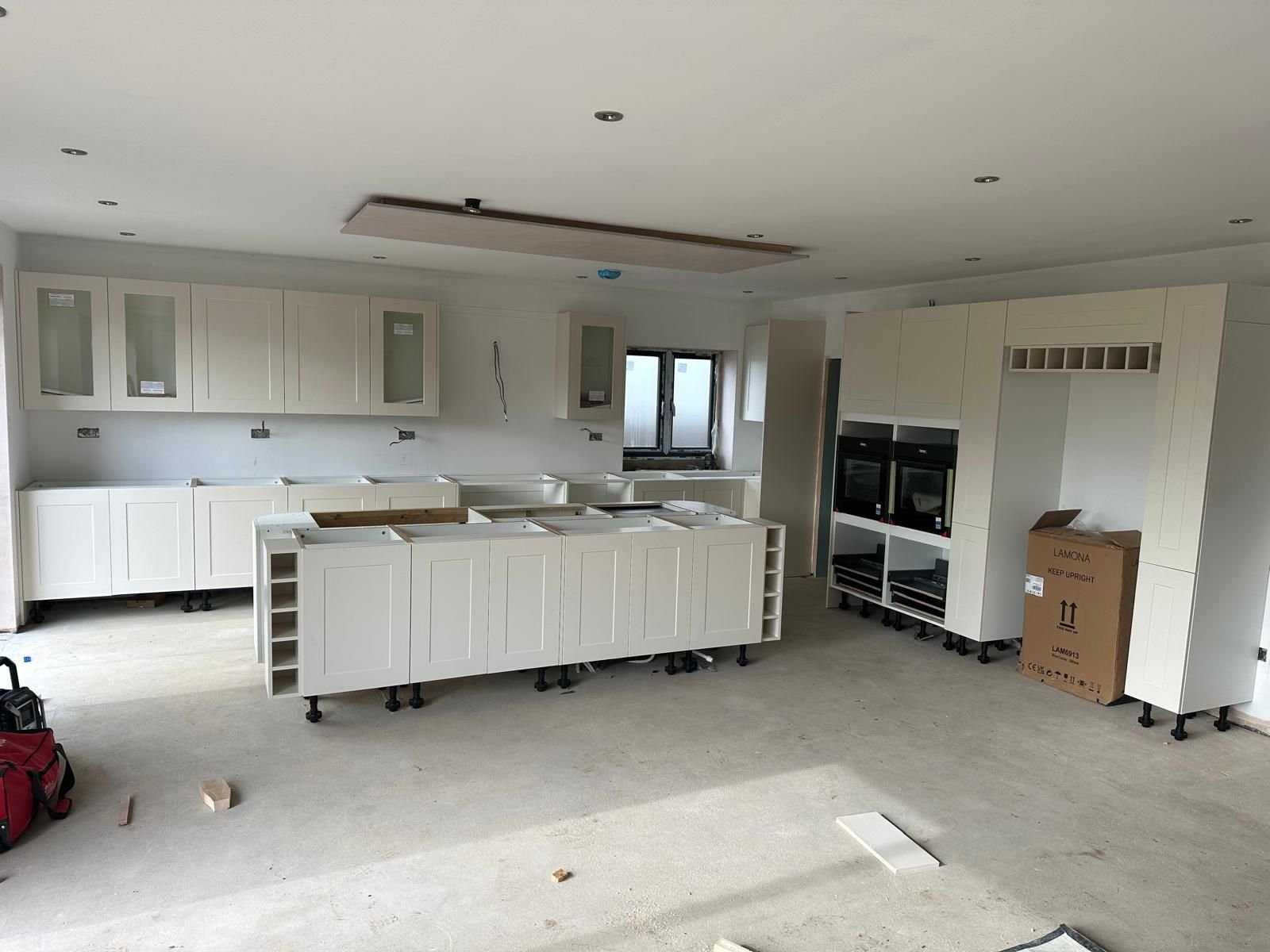 Under construction kitchen with white cabinets, black appliances, and a window, with construction tools and debris on the floor.  Carpentry, construction and Renovation by DA Build in London, Surrey and Greater London.