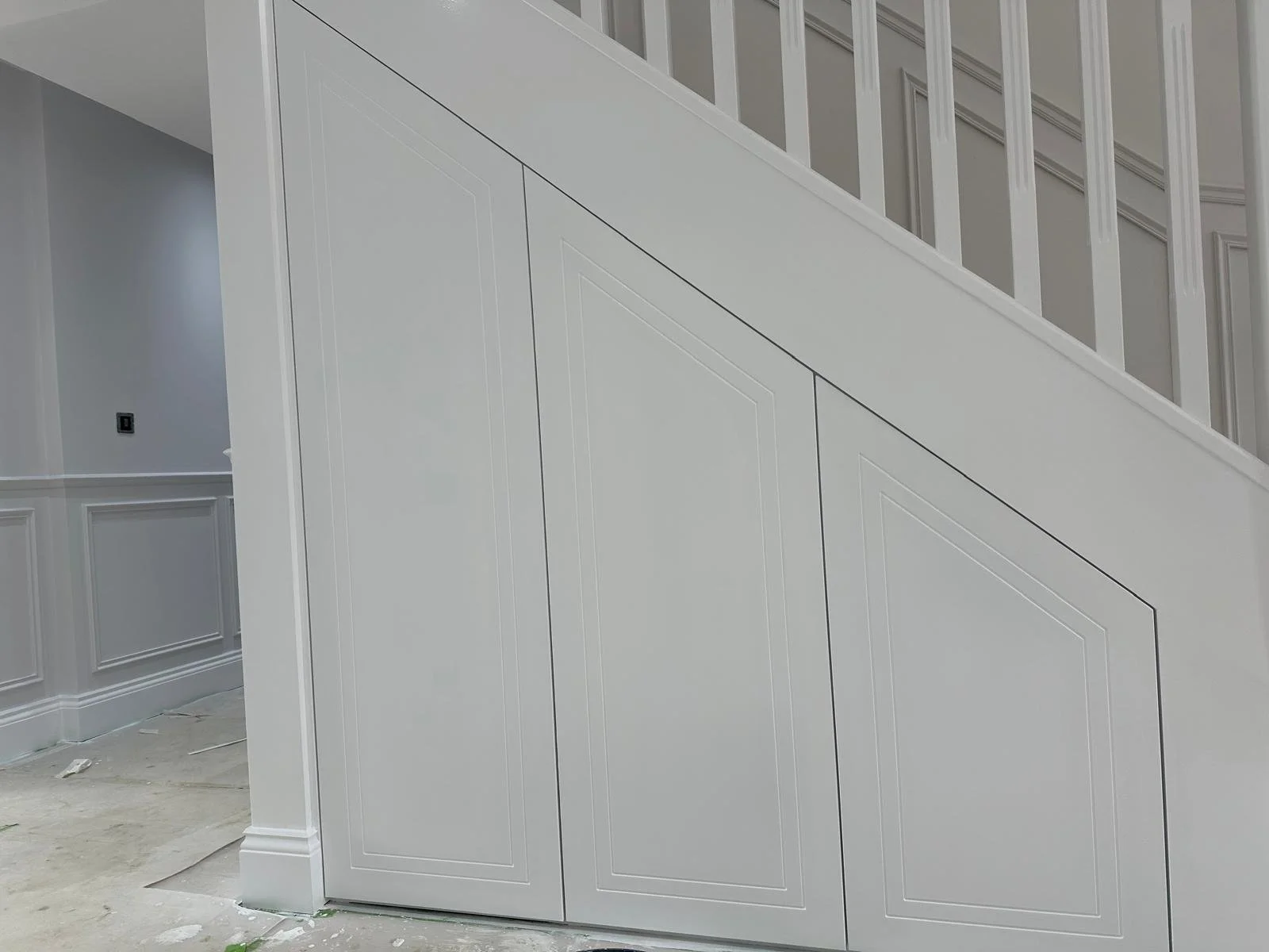 Interior view of a white staircase with decorative paneling on the lower part of the wall, and a small section of wainscoting.  Carpentry, construction and Renovation by DA Build in London, Surrey and Greater London.
