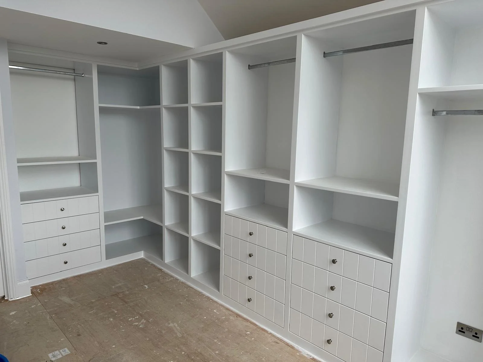 White custom-built closet with open shelving, drawers, and hanging rods in an unfinished room.  Carpentry, construction and Renovation by DA Build in London, Surrey and Greater London.