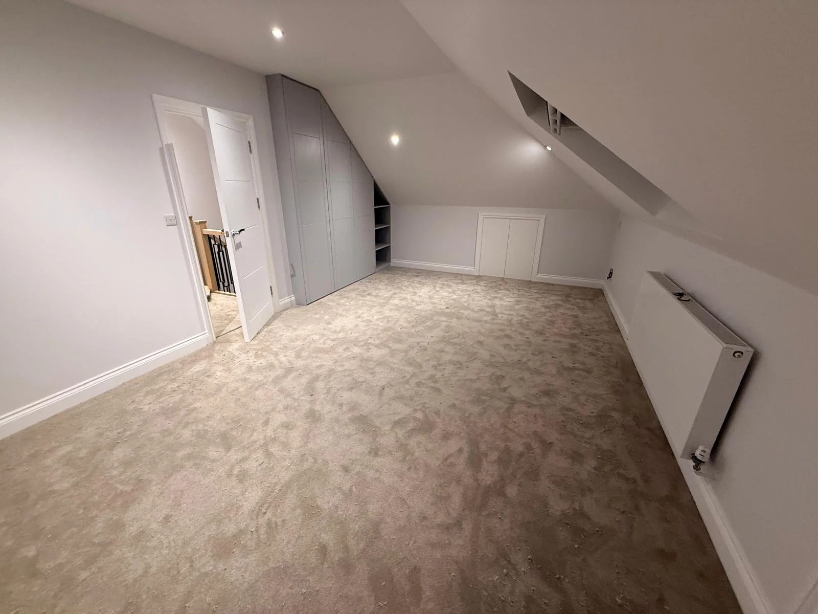 Attic room with beige carpet, white walls, sloped ceiling, built-in storage, and a radiator.  Carpentry, construction and Renovation by DA Build in London, Surrey and Greater London.