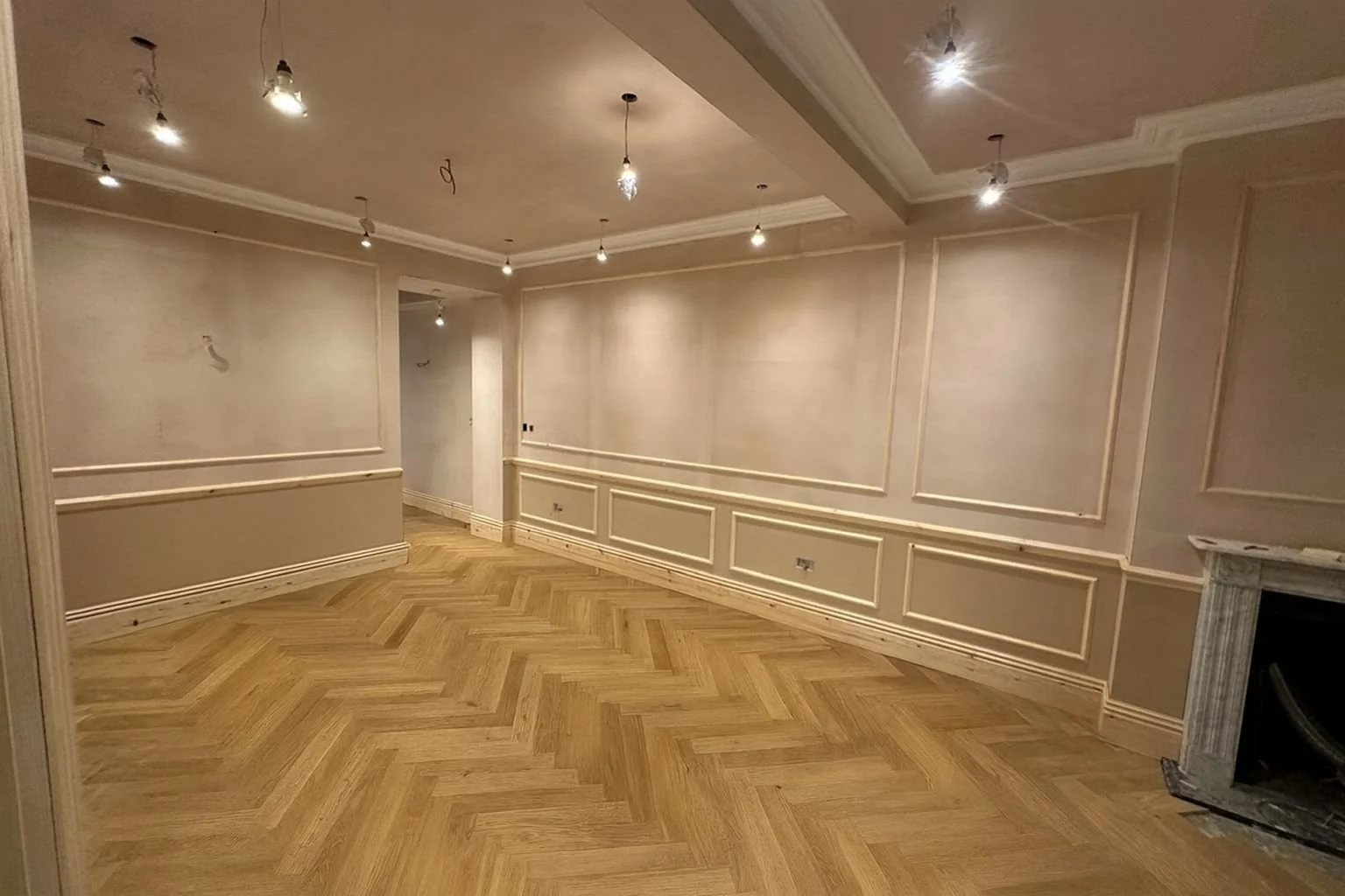 Interior of a room under renovation with beige walls, detailed molding, and a wooden herringbone pattern floor.  Carpentry, construction and Renovation by DA Build in London, Surrey and Greater London.