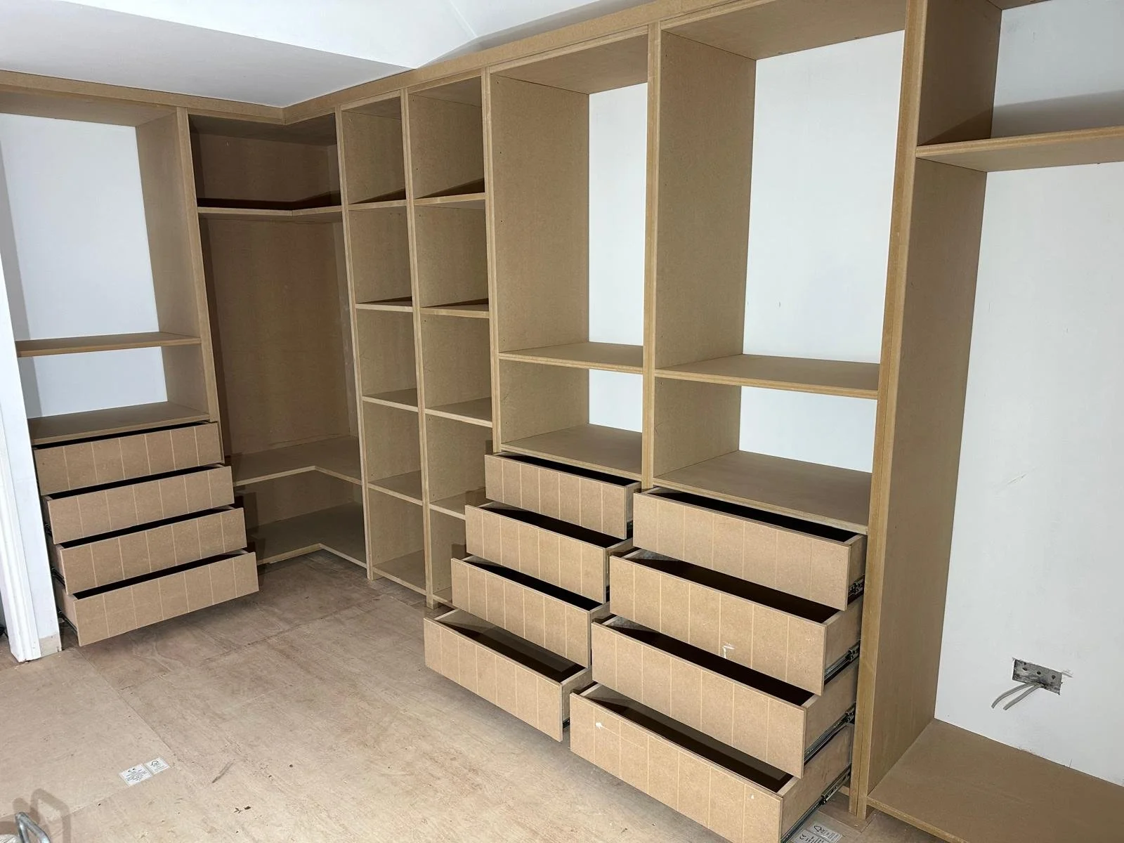 Empty custom wood shelving unit with open drawers in a room under construction. Carpentry and Renovation by DA Build in London, Surrey and Greater London.