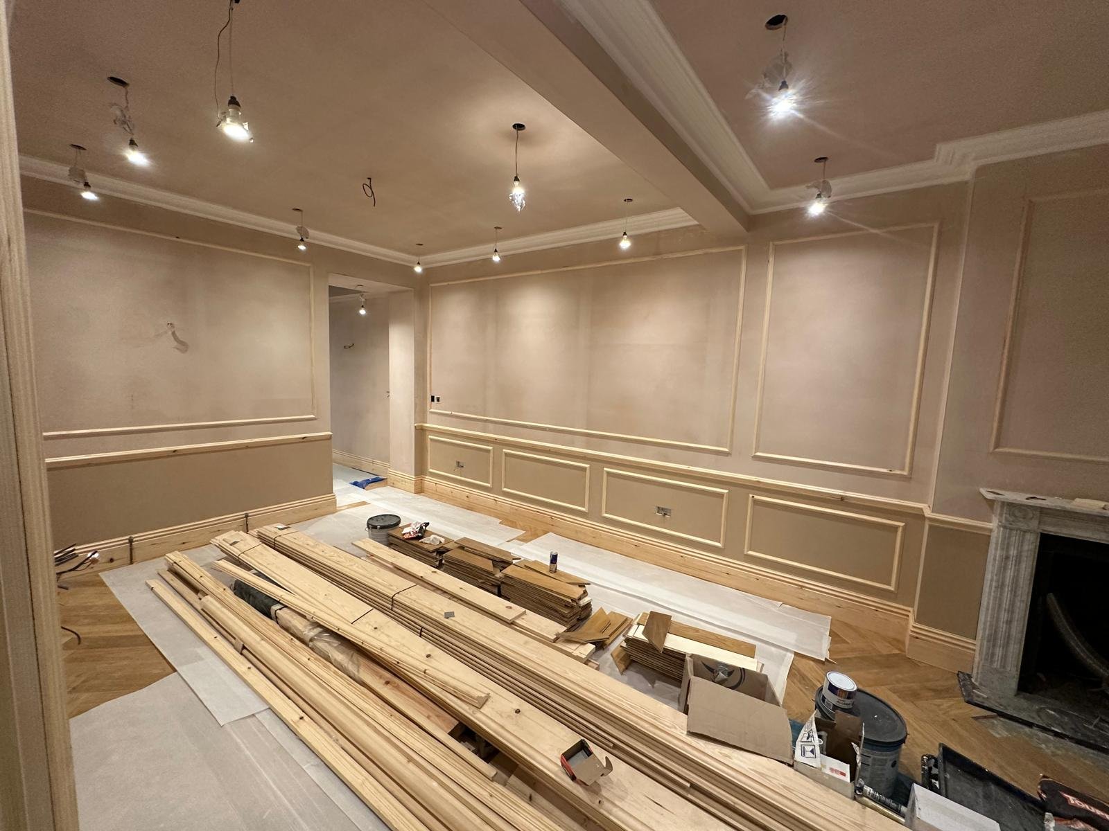 Interior of a room under renovation with unfinished ceiling lights, beige walls with decorative molding, and wooden building materials and tools on the floor. Carpentry, construction and Renovation by DA Build in London, Surrey and Greater London.