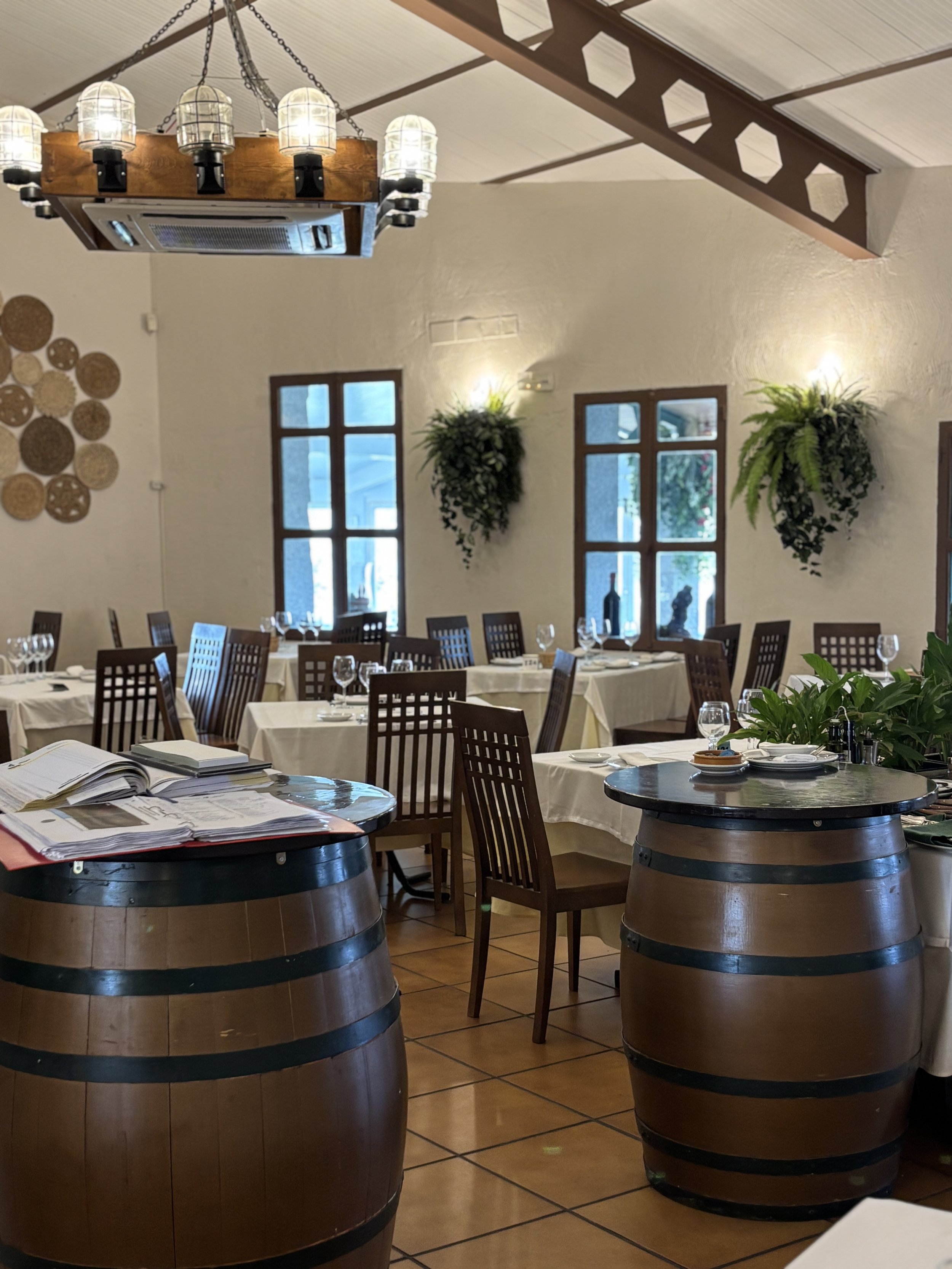 Interiores de un restaurante con mesas arregladas, jarras de vino, y decoración de paredes con plantas y objetos decorativos en la pared.