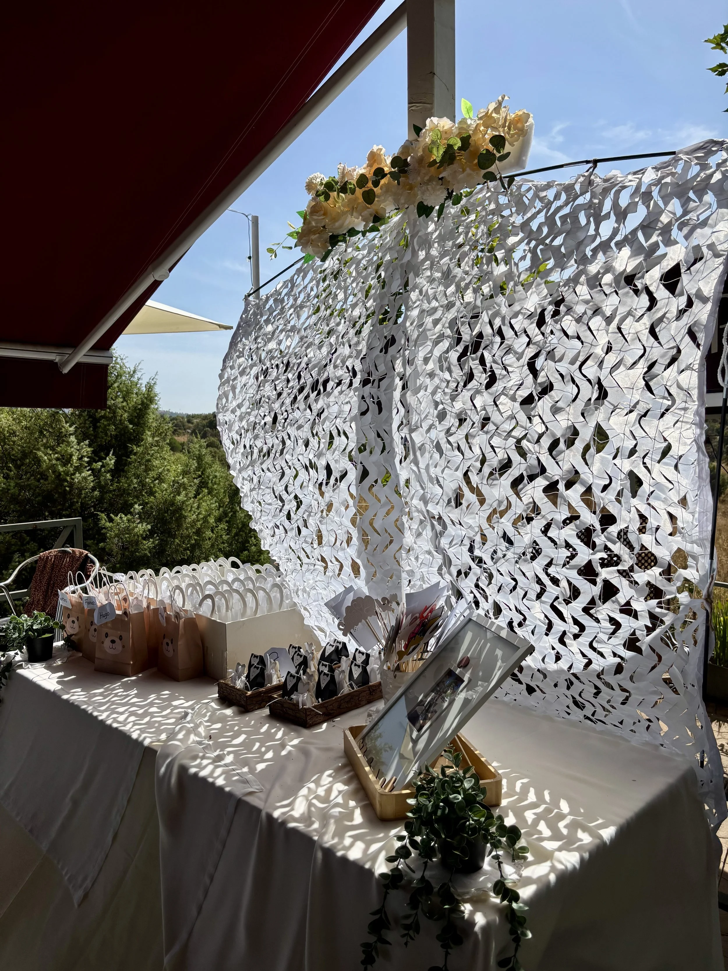 Mesa decorada con regalos pequeños con cara de oso, fotografías, plantas suculentas, y decoración en blanco y negro. Al fondo, un mural de papel de patrón recortado y plantas verdes.