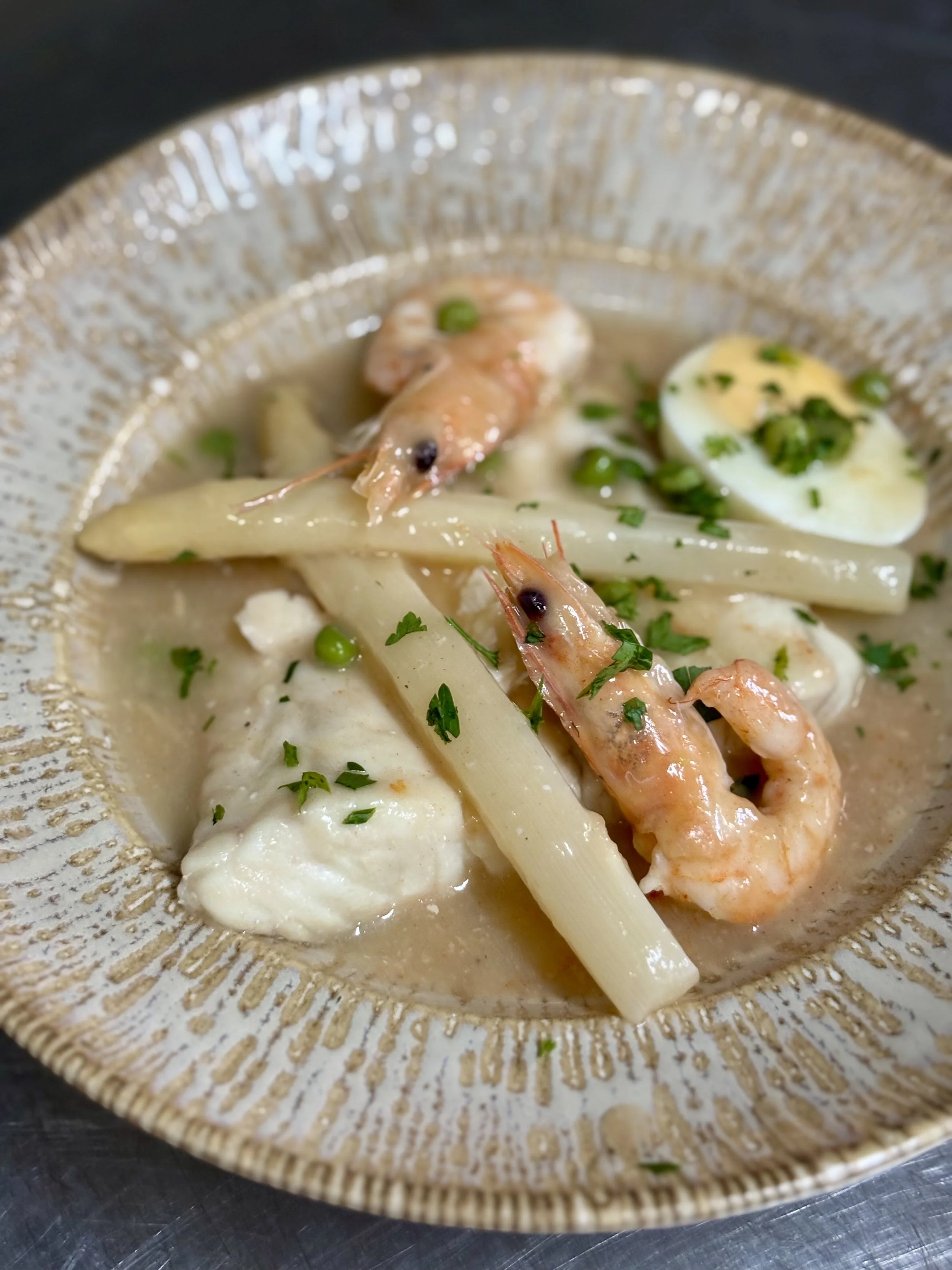 Camaron con pasta, huevo cocido y verduras en sopa cremosa en tazón decorado con perejil.