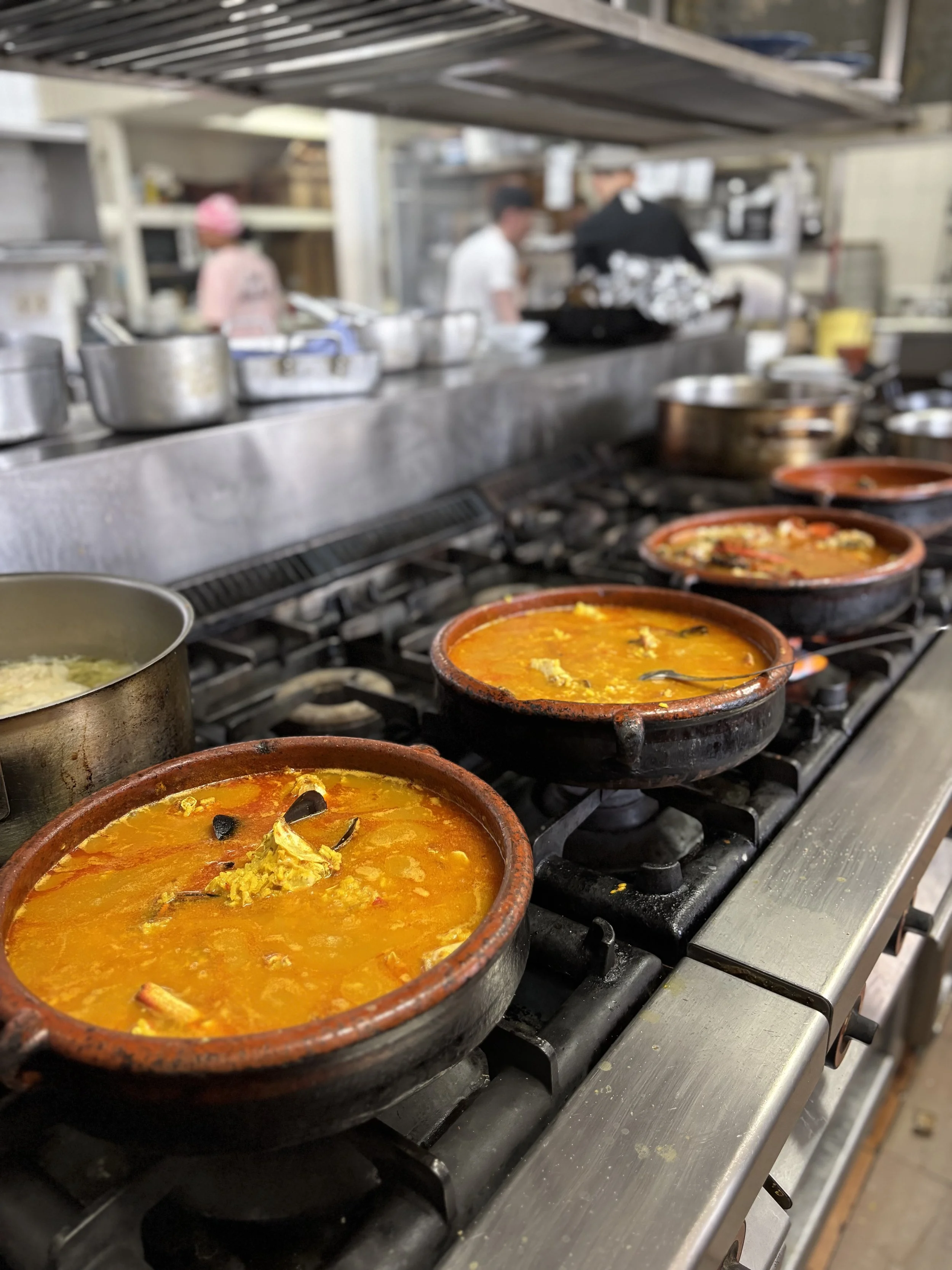 Ollas de barro con diferentes guisos sobre una estufa industrial en una cocina de restaurante.