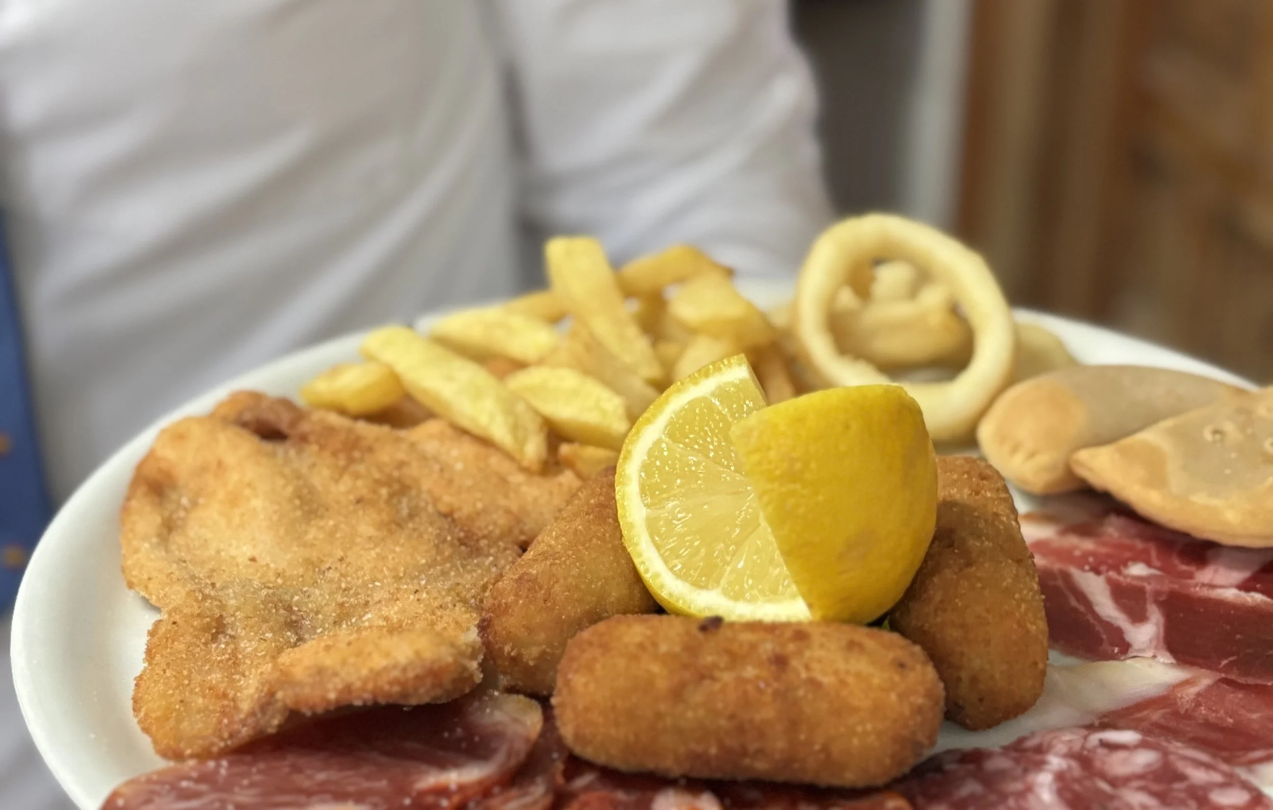 Plato de comida con filetes empanizados, papas fritas, rodajas de limón, calamares y diferentes tipos de carne.