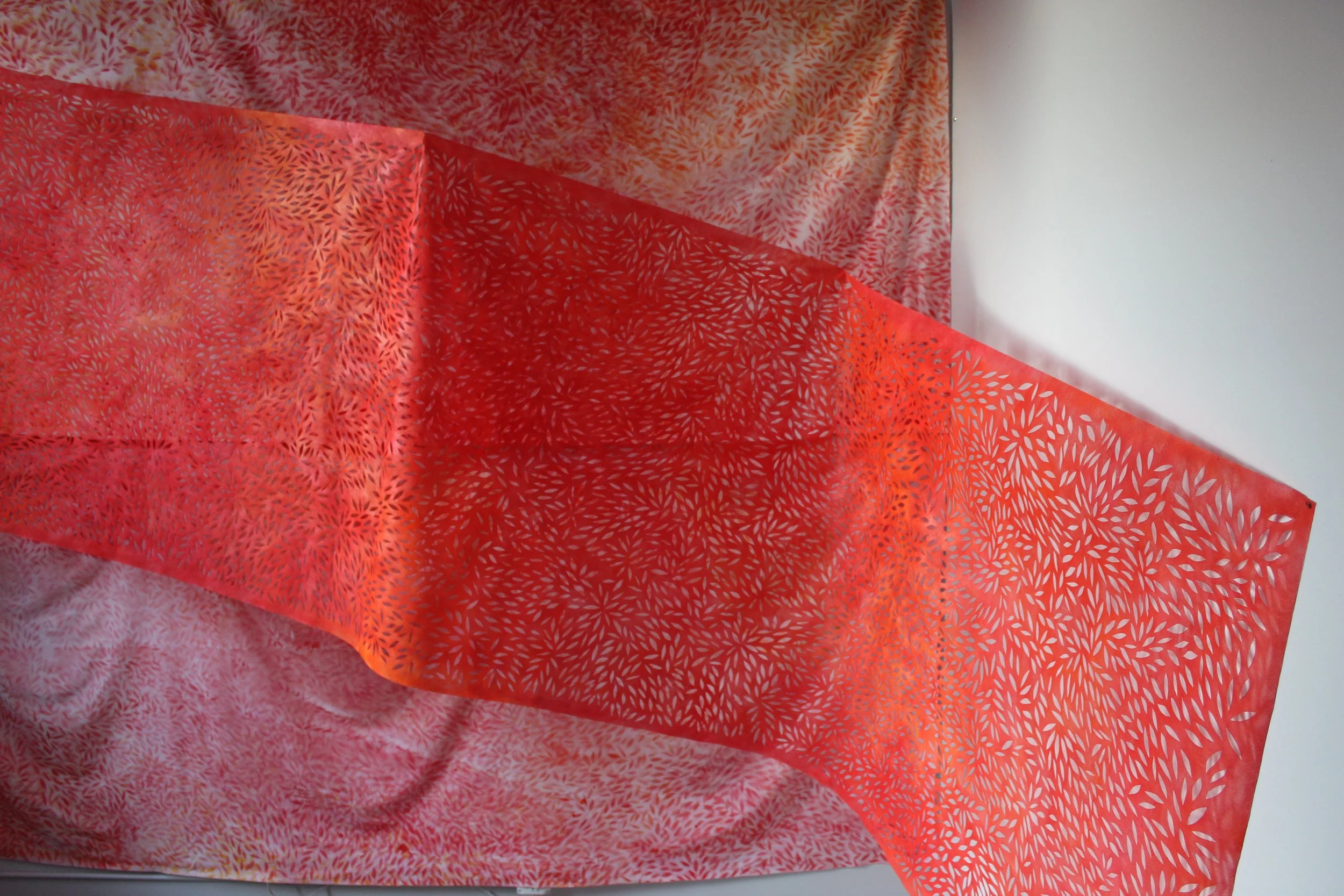 A red fabric with leaf patterns draped over a white surface with a similar patterned background.