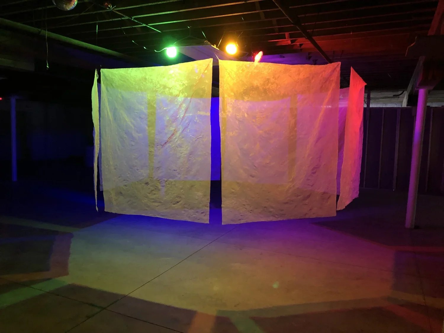 Colorful translucent fabric hanging from the ceiling with colored lights casting rainbow patterns on the floor.