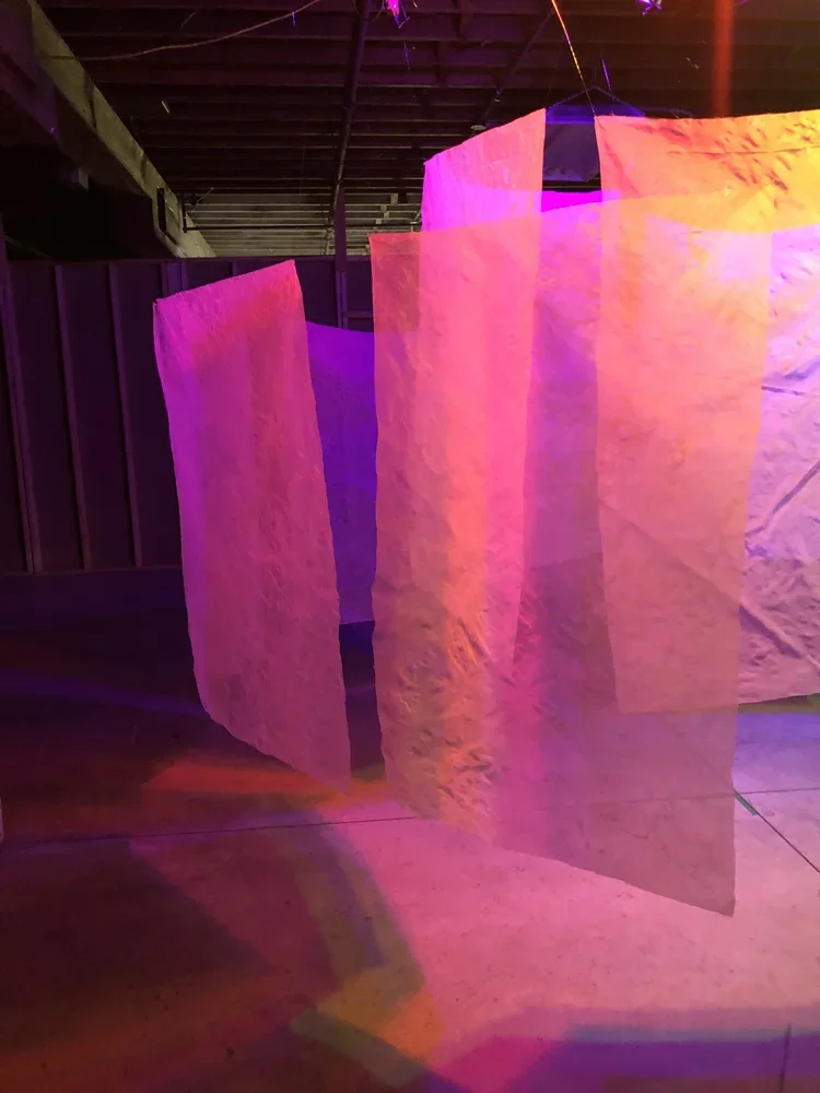 Decorative hanging paper lanterns illuminated with pink, purple, and orange lighting, hanging indoors.
