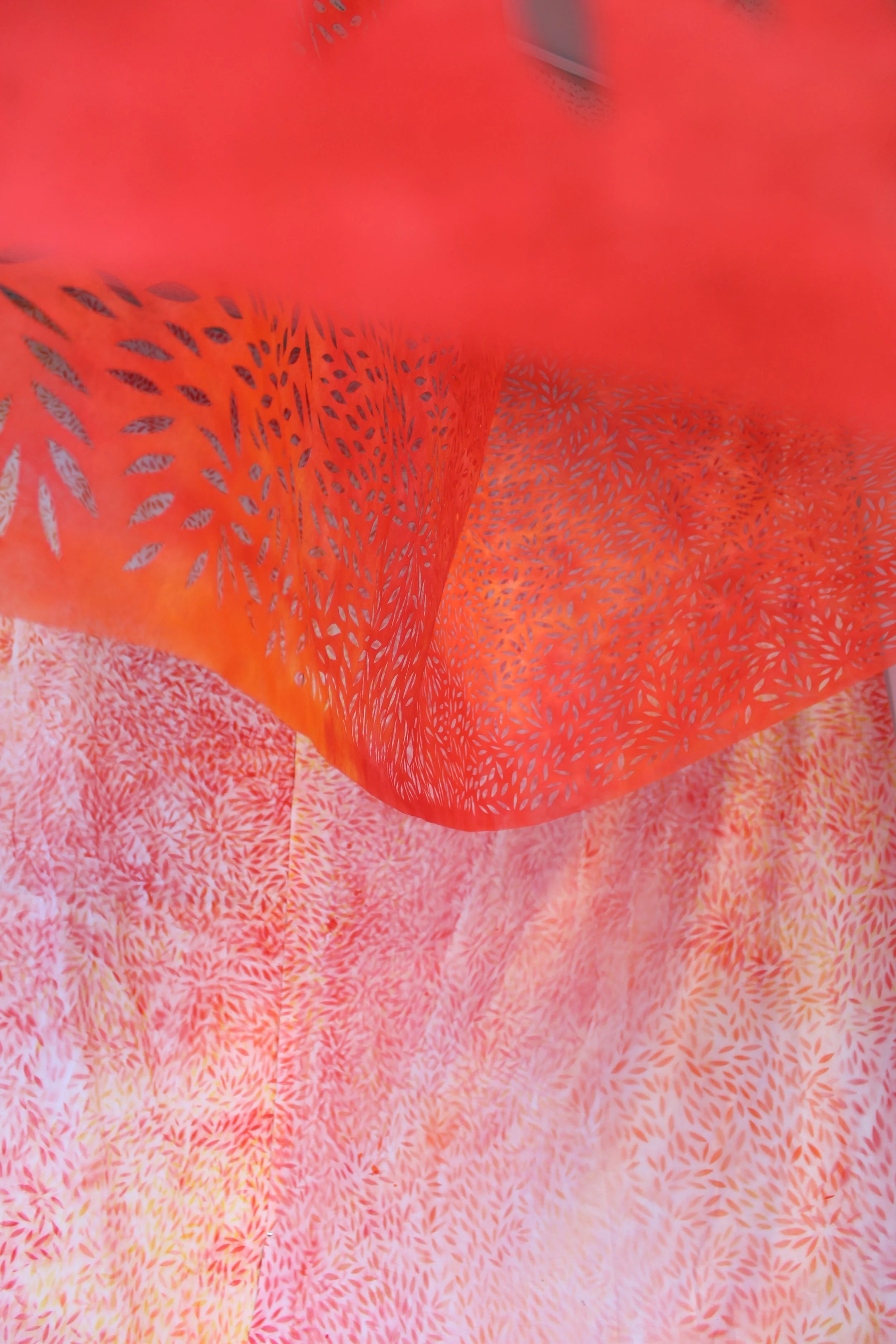 Close-up view of an orange paper lantern with intricate cut-out leaf patterns, surrounded by pink and orange textured fabric.