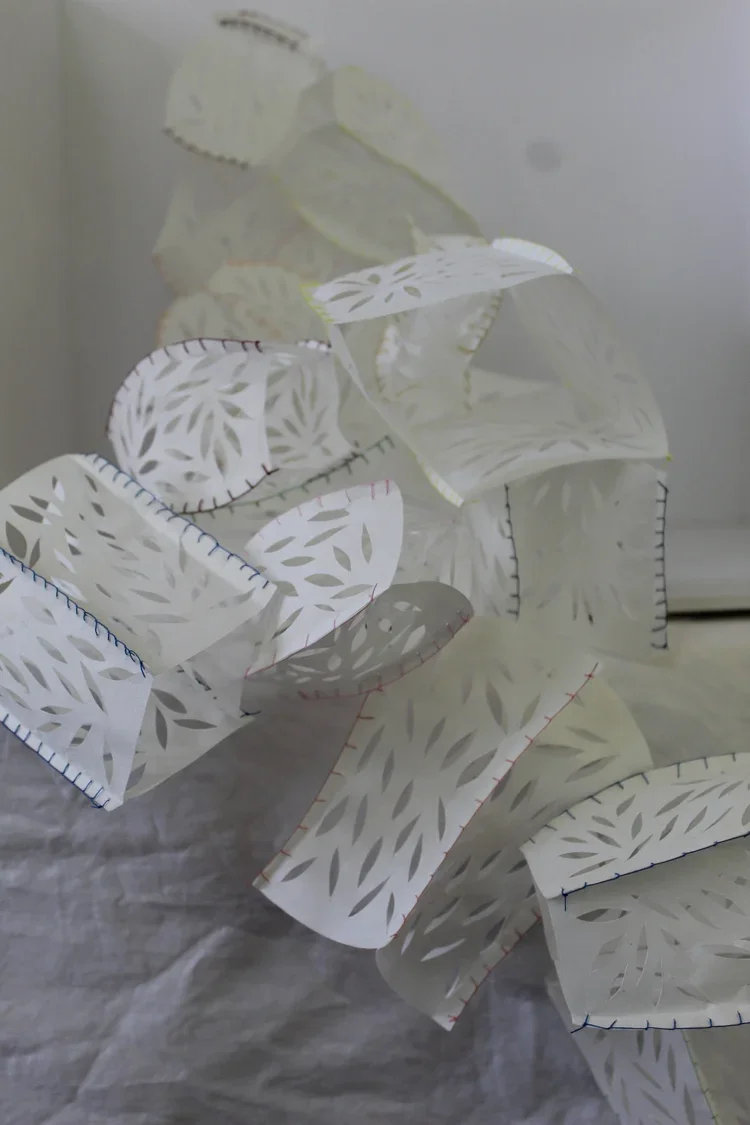 Close-up of white paper lanterns with leaf-like cutout patterns and stitched edges.