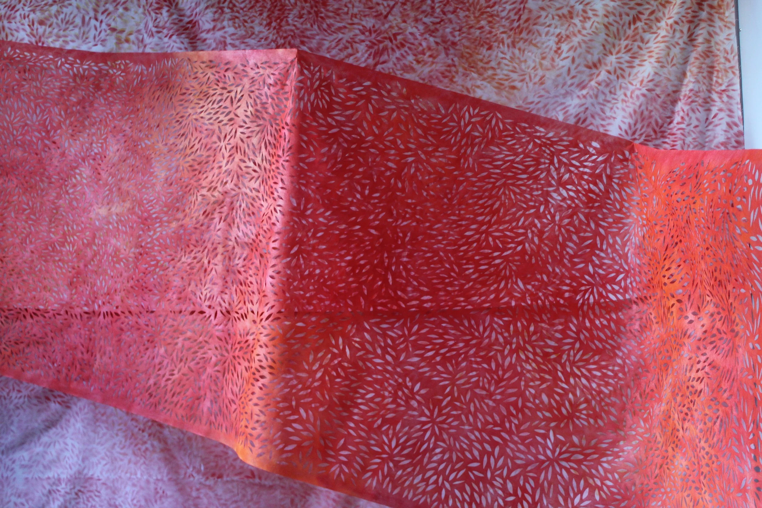 A piece of fabric with red and pink leaf-like patterns, draped on a similar patterned background.