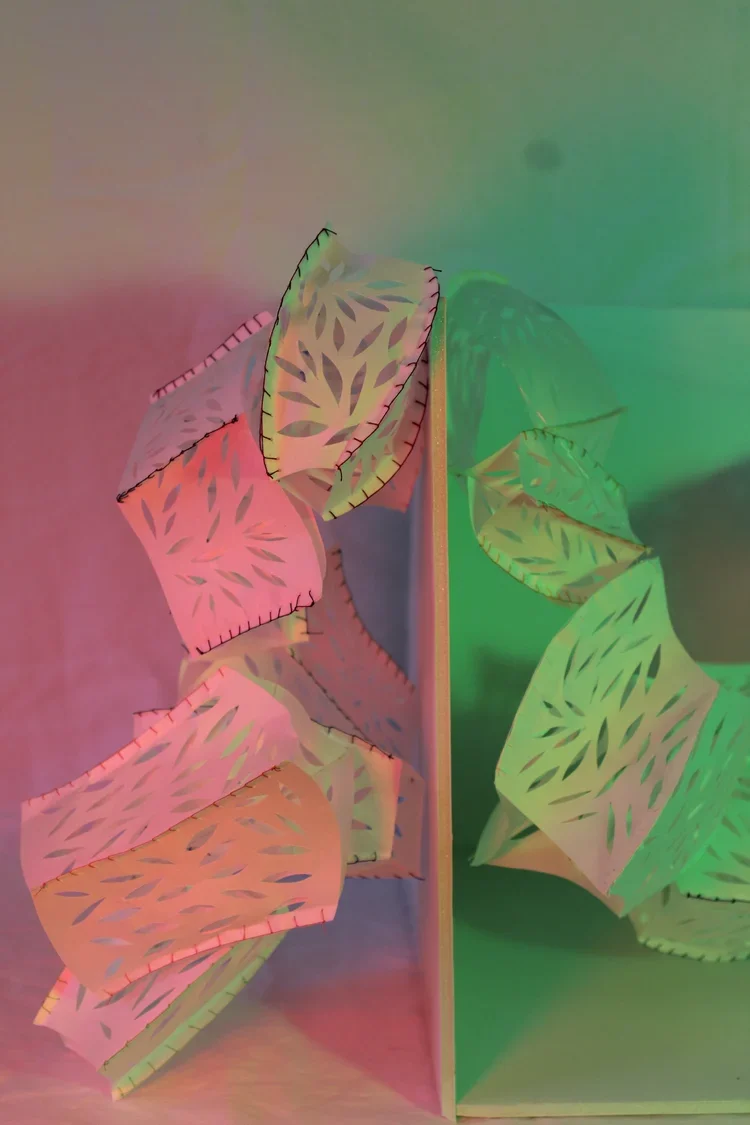 Colorful paper pieces with leaf-like cutout patterns arranged in a collage, with a split green background.