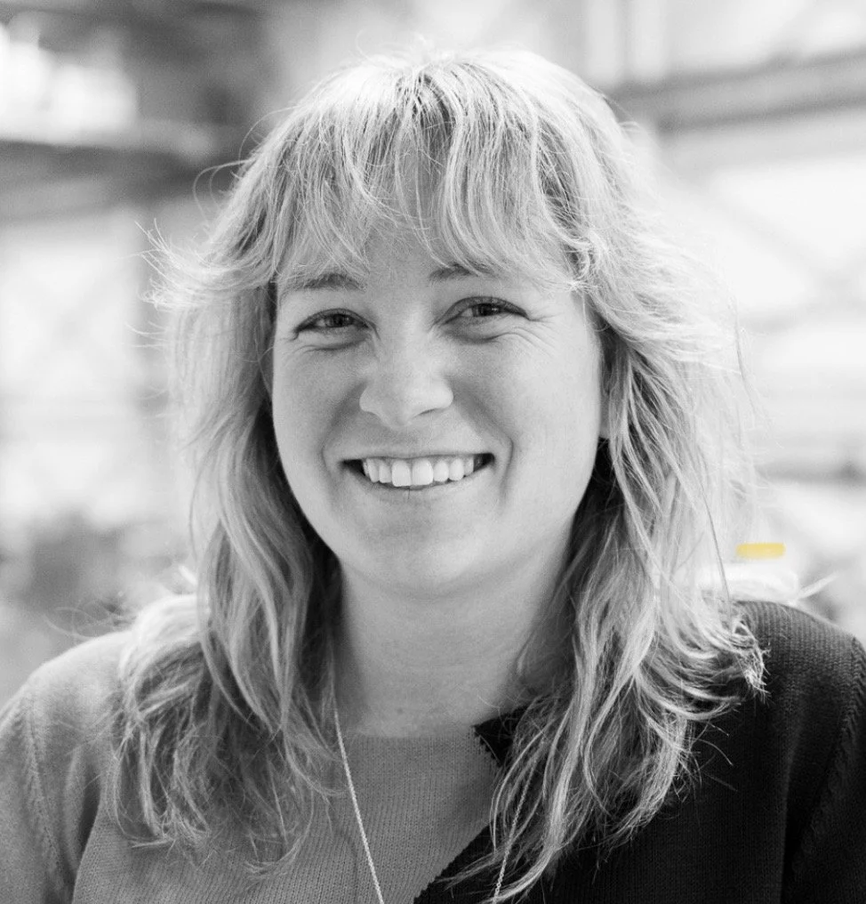 A smiling woman with long, wavy hair in black and white, in an indoor setting.