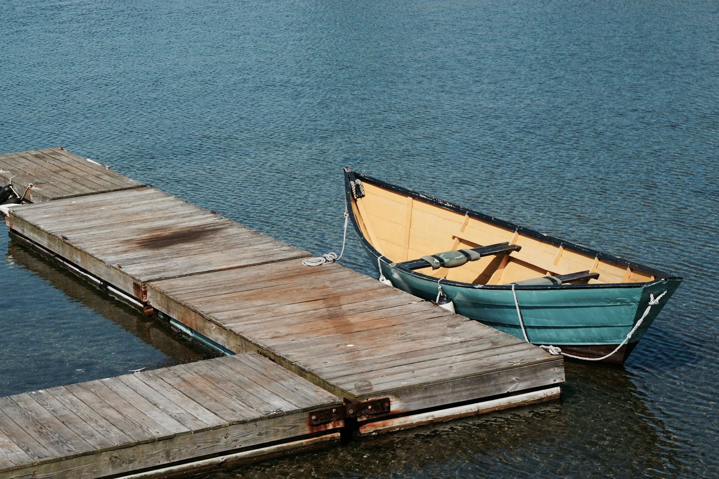 A small green and beige rowboat docked at a wooden pier on calm water.