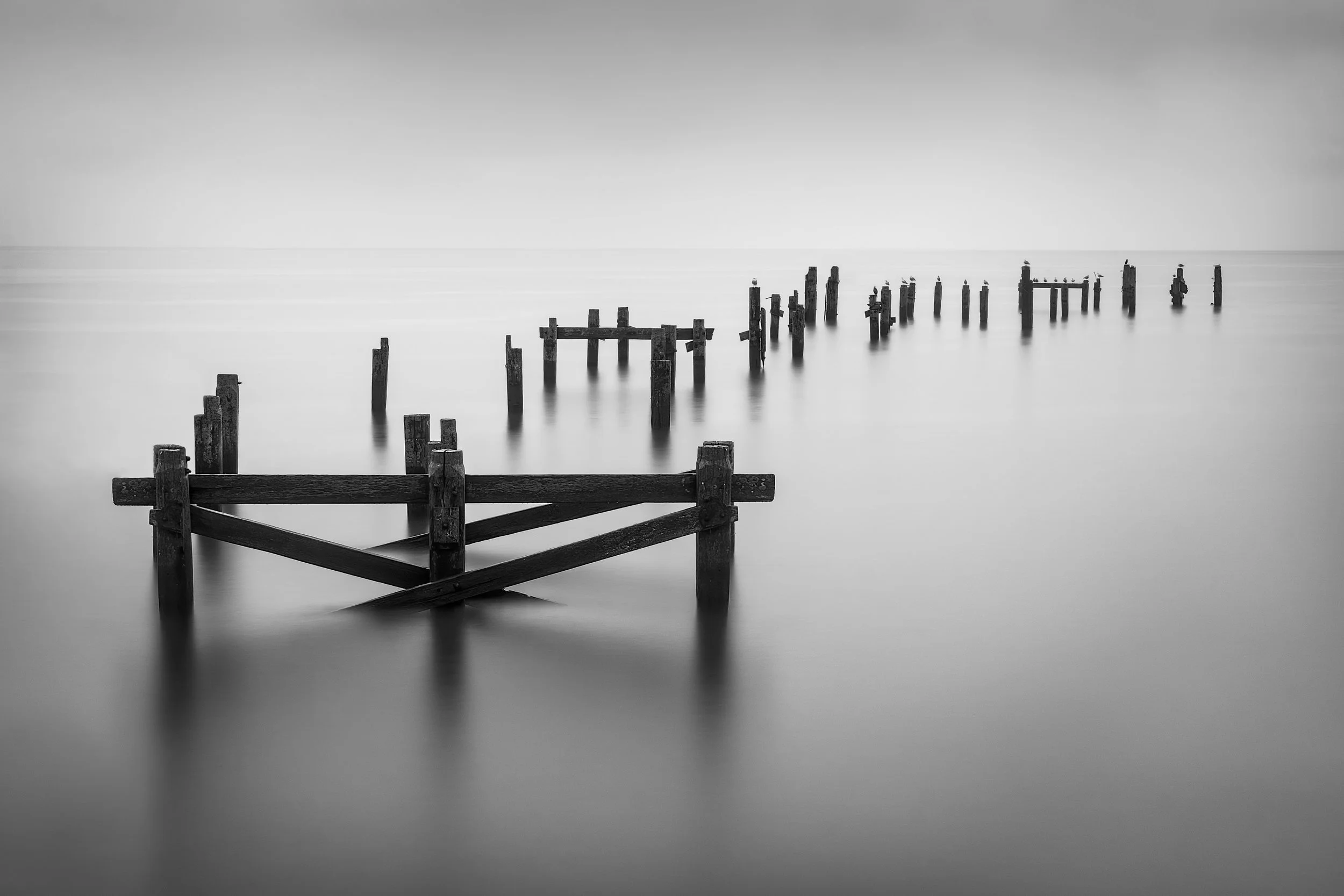 Remains of Swanage Old Pier extending into calm water, with weathered timber posts fading towards a hazy horizon.
