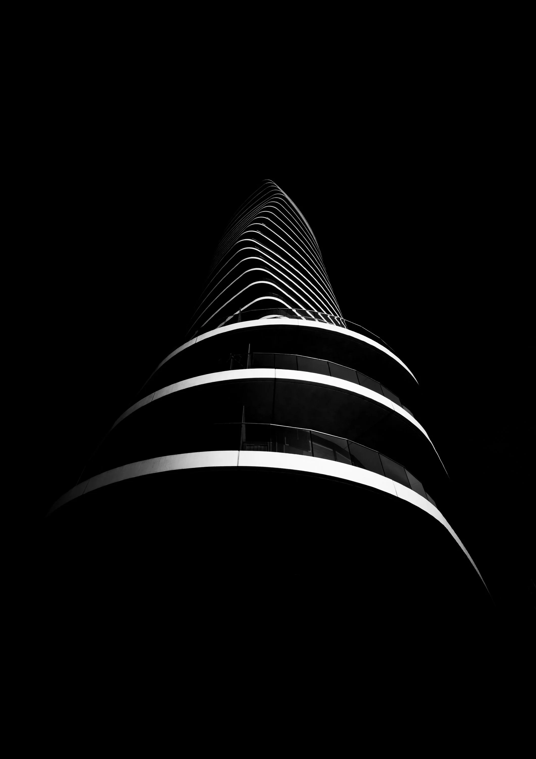 Lombard Wharf in Battersea viewed from below at night, its curved tower defined by illuminated horizontal bands.