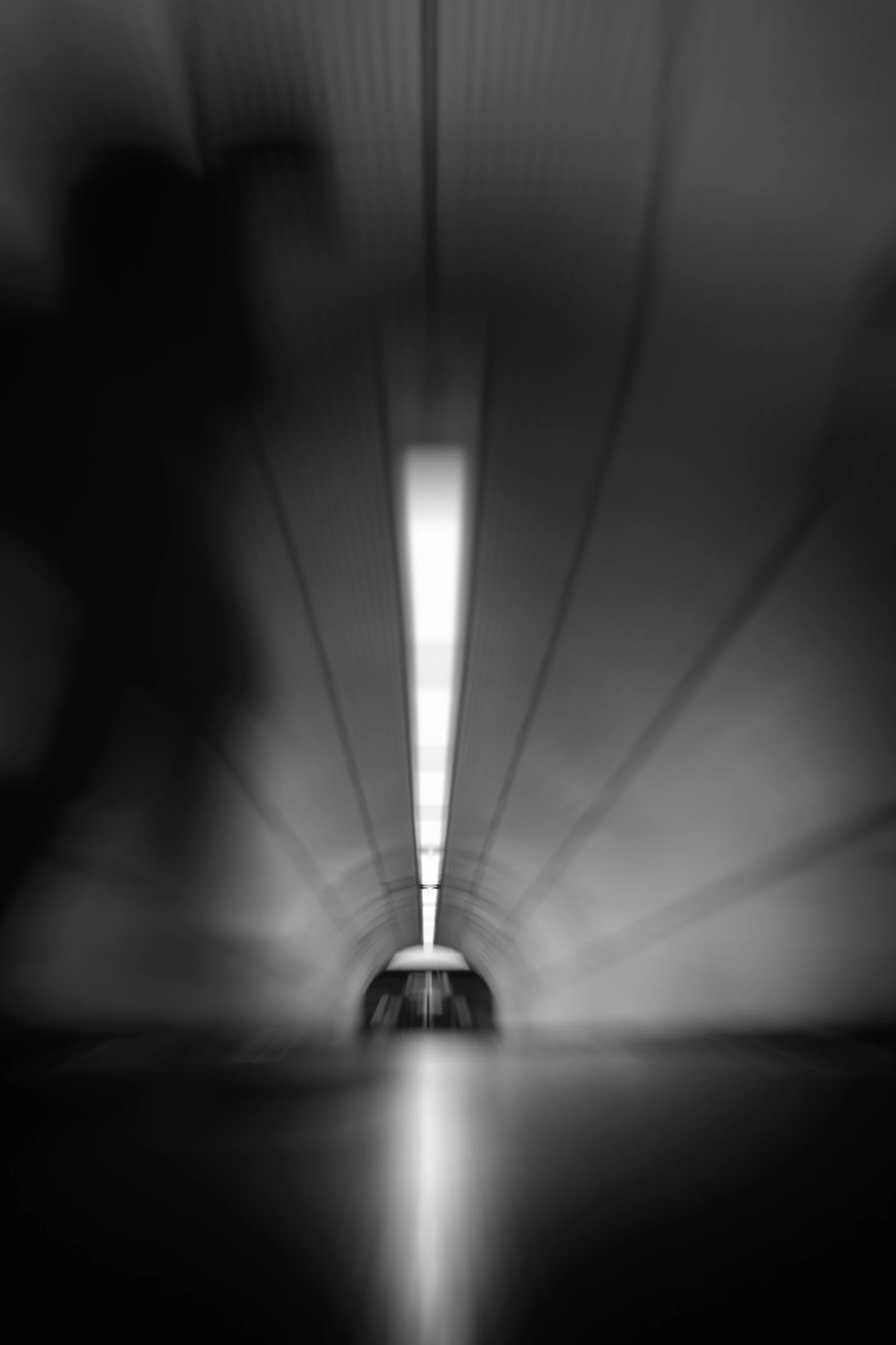 Curved passageway at Bond Street Elizabeth line station, leading towards a bright opening reflected on the floor.
