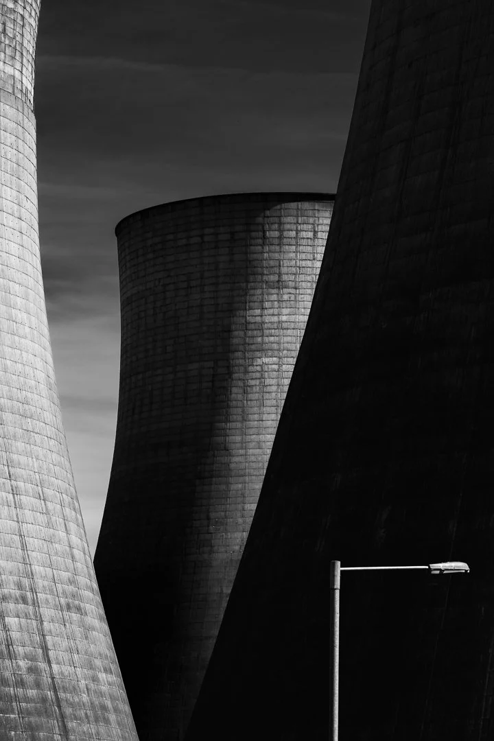 Dramatic shadows between the curved concrete cooling towers with lamp post for scale at Ratcliffe-on-Soar Power Station, photographed in black and white.