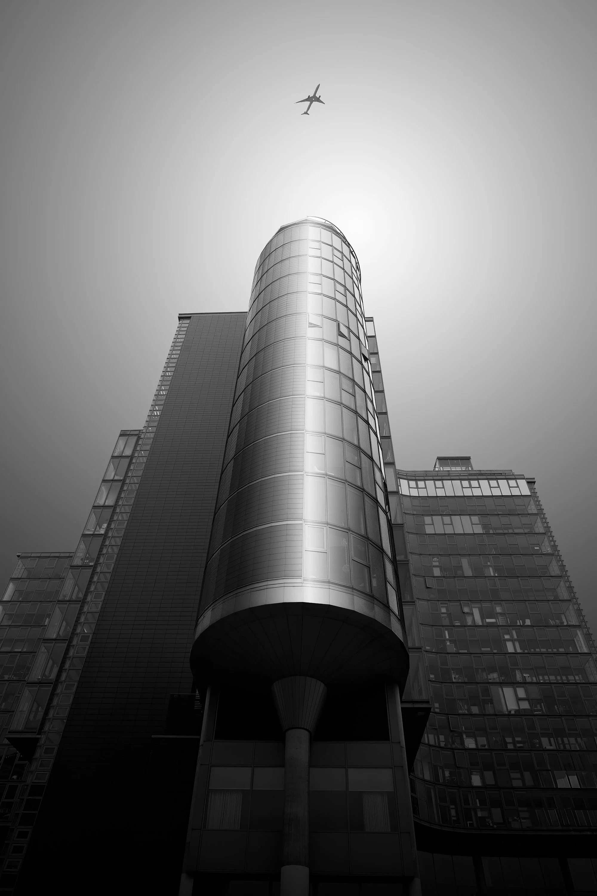 Hotel Rafayel in Battersea viewed from below, its curved glass façade rising into the sky as a plane passes overhead.