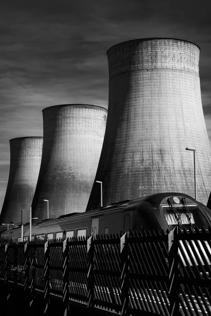 Black-and-white photograph of a railway locomotive beneath the towering concrete cooling towers of Ratcliffe-on-Soar Power Station.