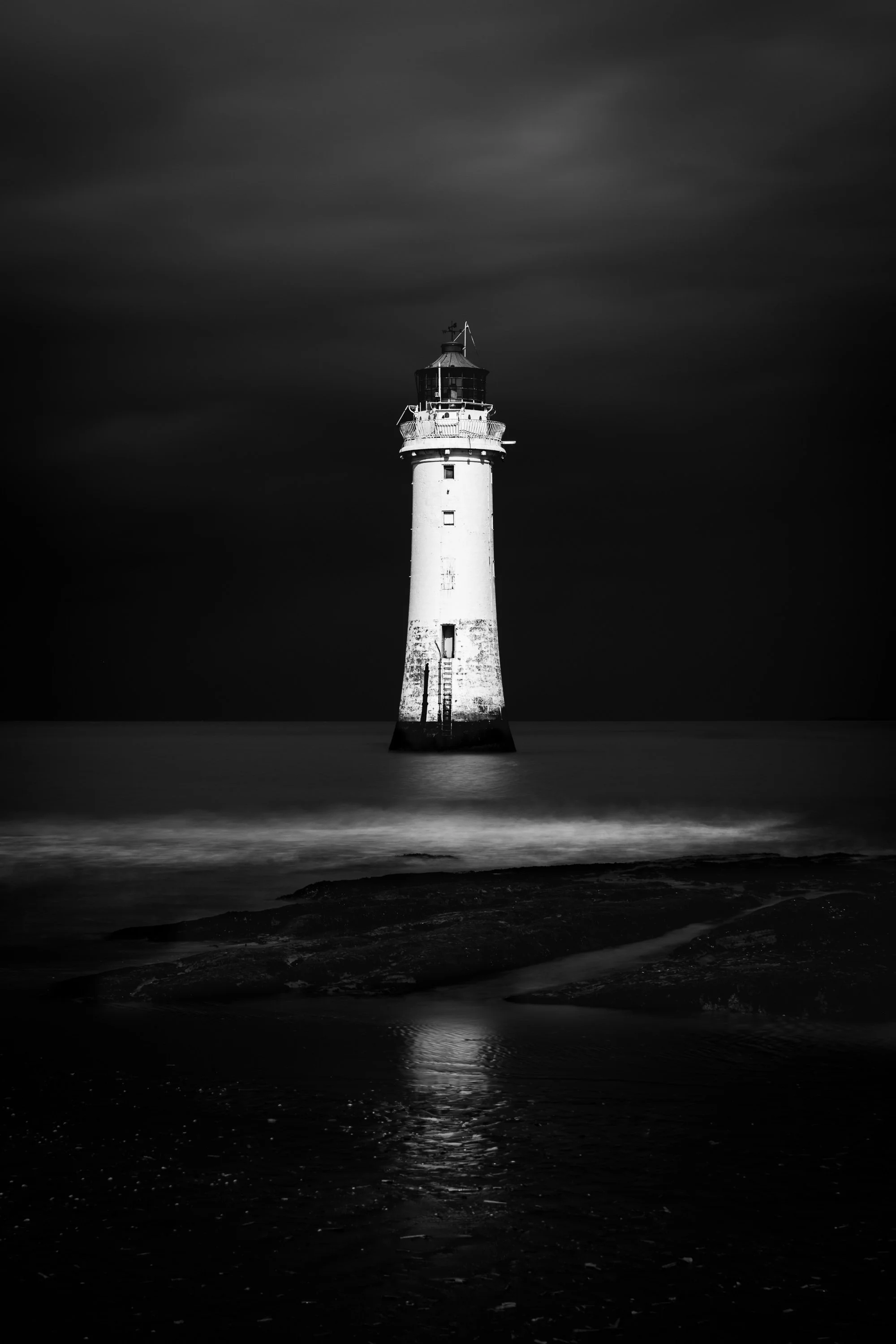 New Brighton Lighthouse isolated against the dark sea and sky, with light reflected on the water.