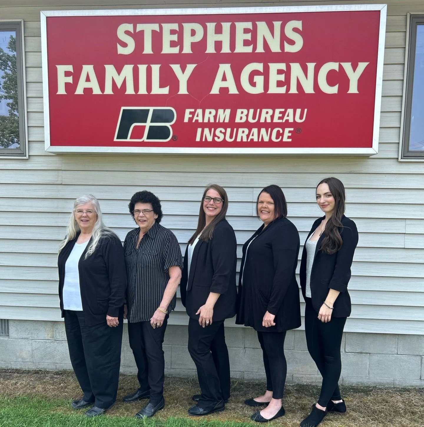Five women standing in front of a building with a red sign reading 'Stephens Family Agency Farm Bureau Insurance'.