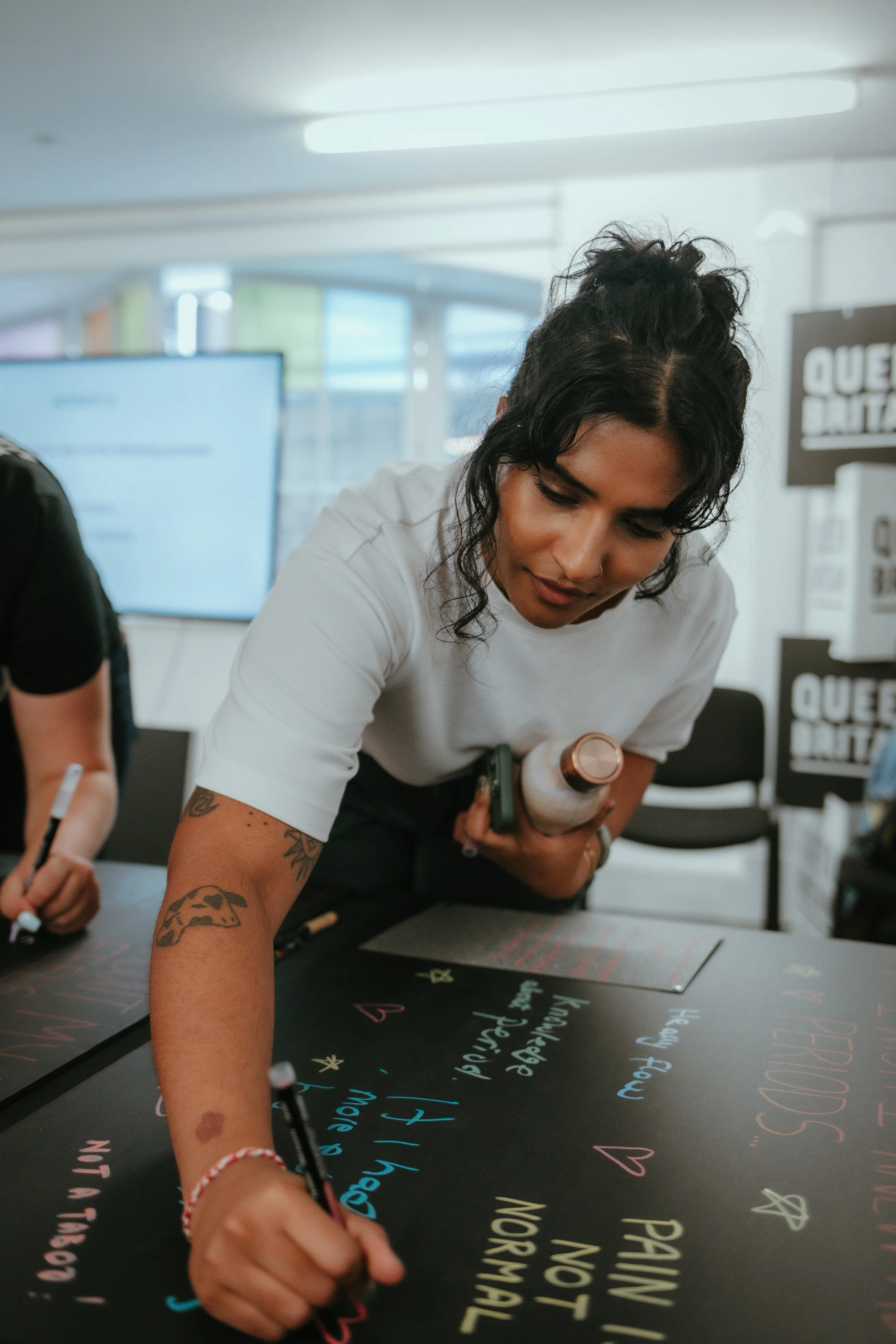 Woman writing colorful messages on a blackboard at an indoor event.