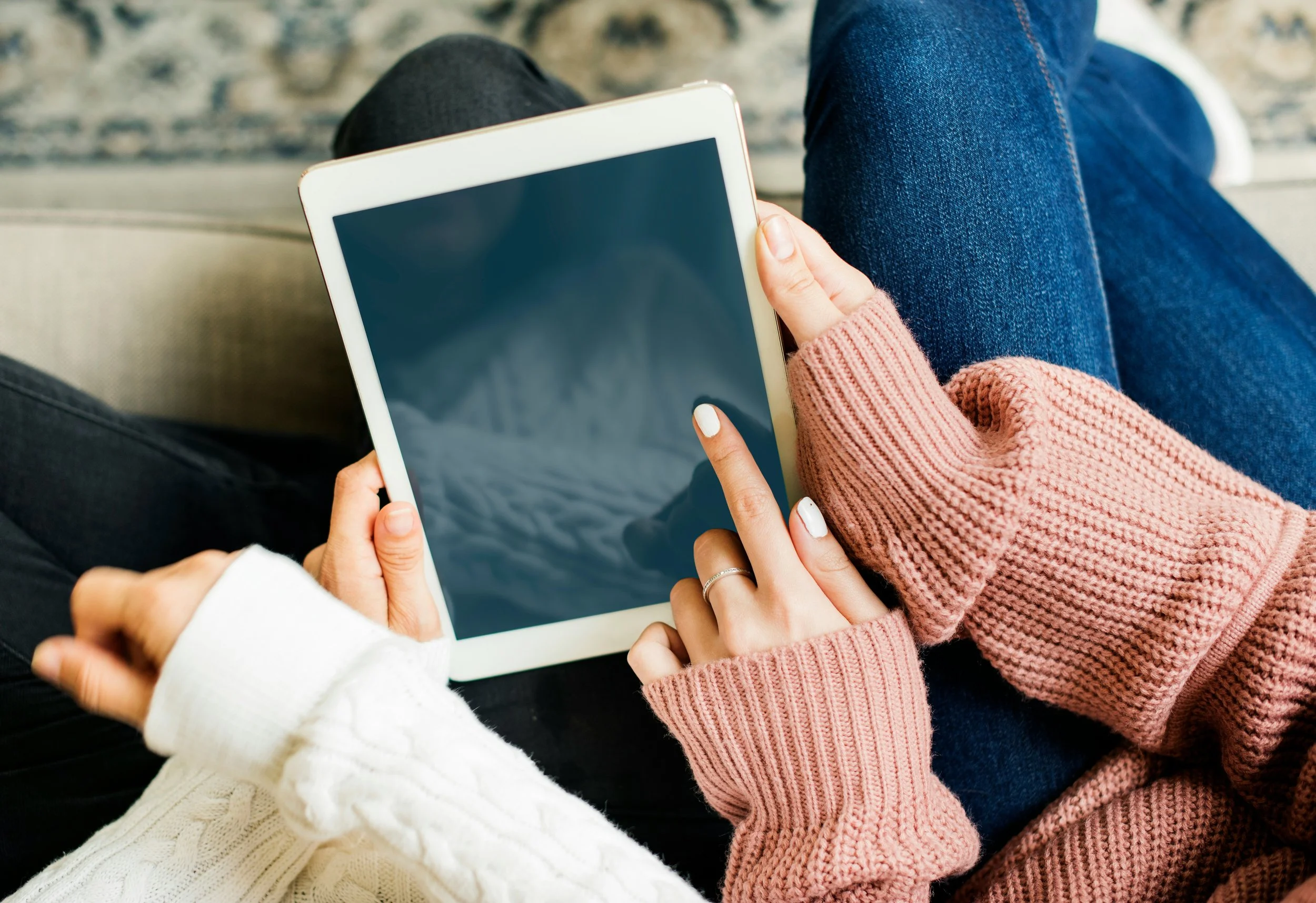 Multiple people sitting together, one holding a tablet with a black screen, dressed in casual clothing including sweaters and jeans.