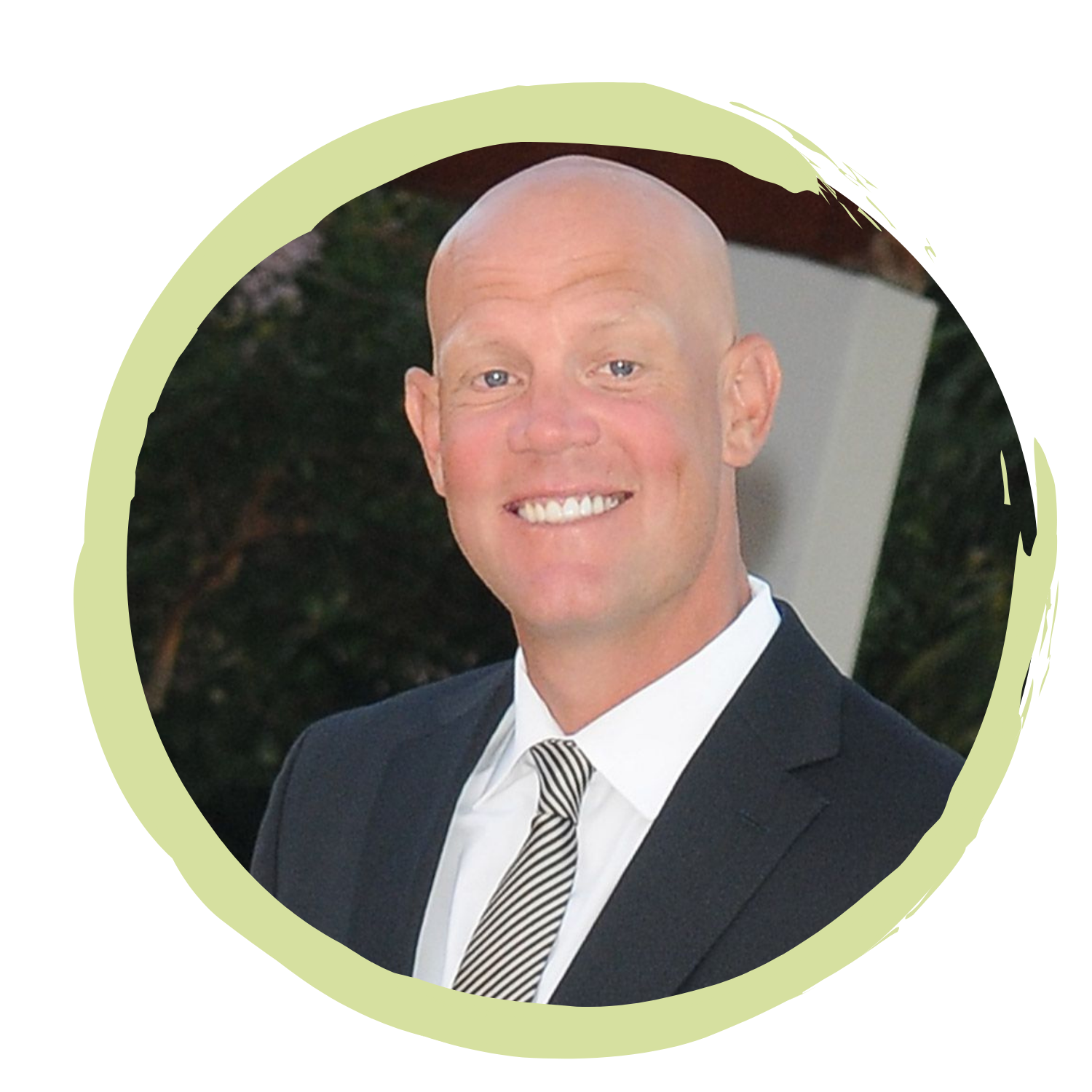 A man with a shaved head and blue eyes wearing a suit and striped tie, smiling outdoors.