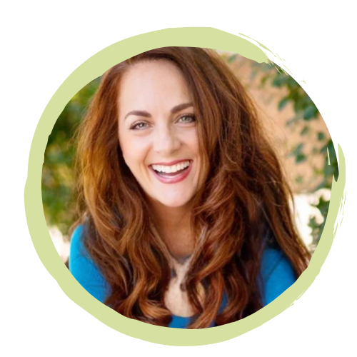 A woman with long, wavy red hair smiling outdoors, wearing a blue top.