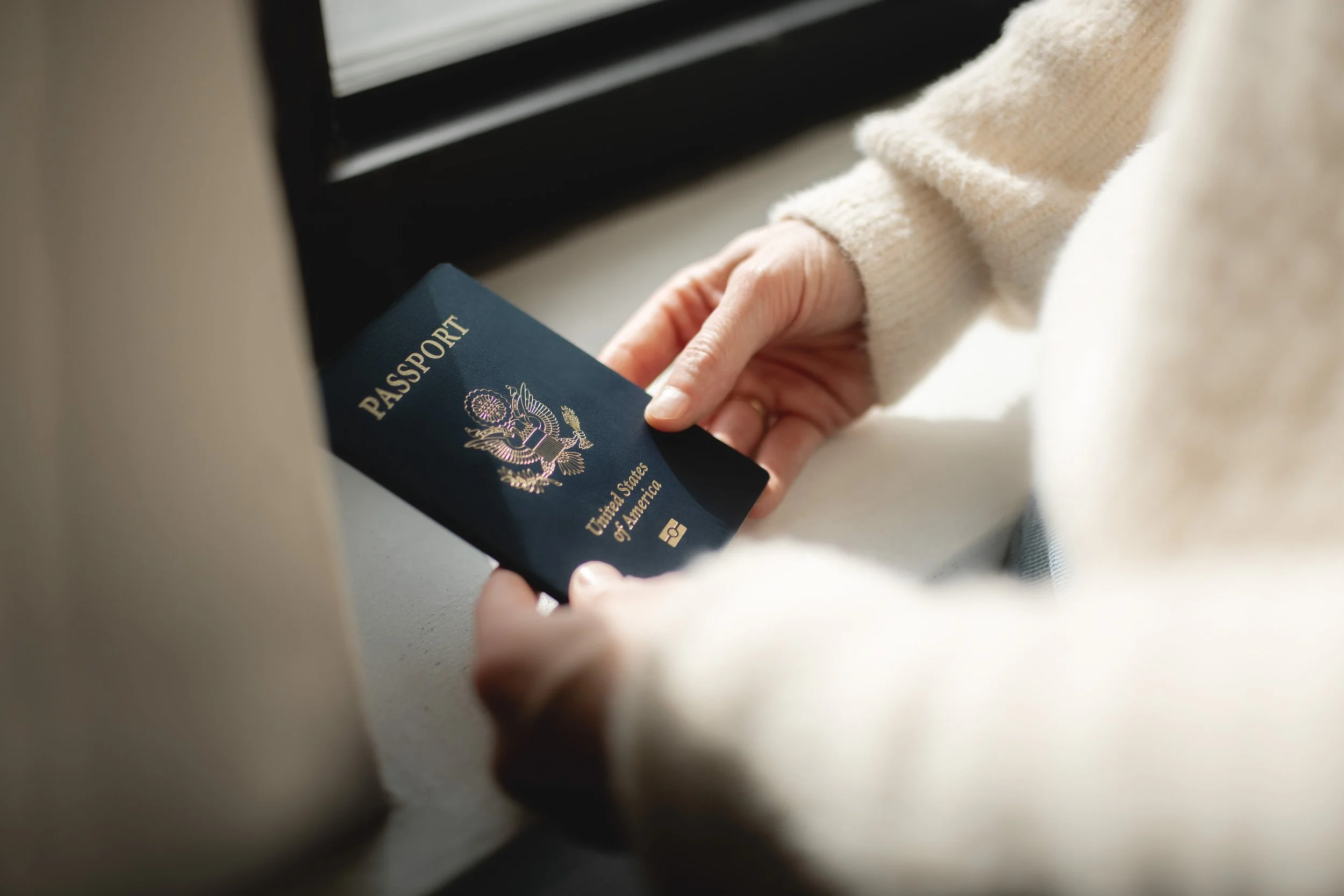 Person holding a U.S. passport near a window.