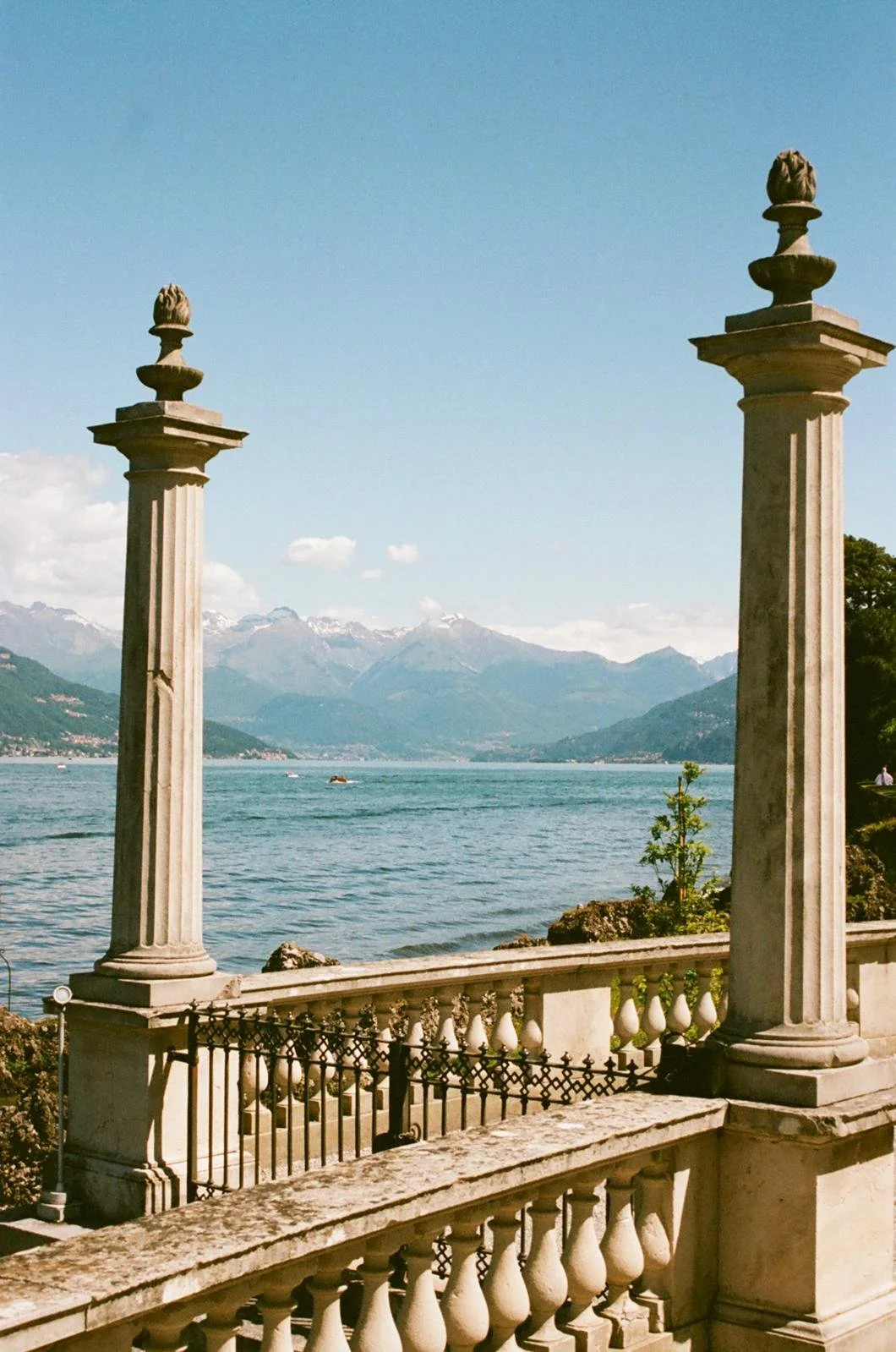 A scenic view of a lake with mountains in the background, framed by two classical stone columns and a decorative stone railing in the foreground.