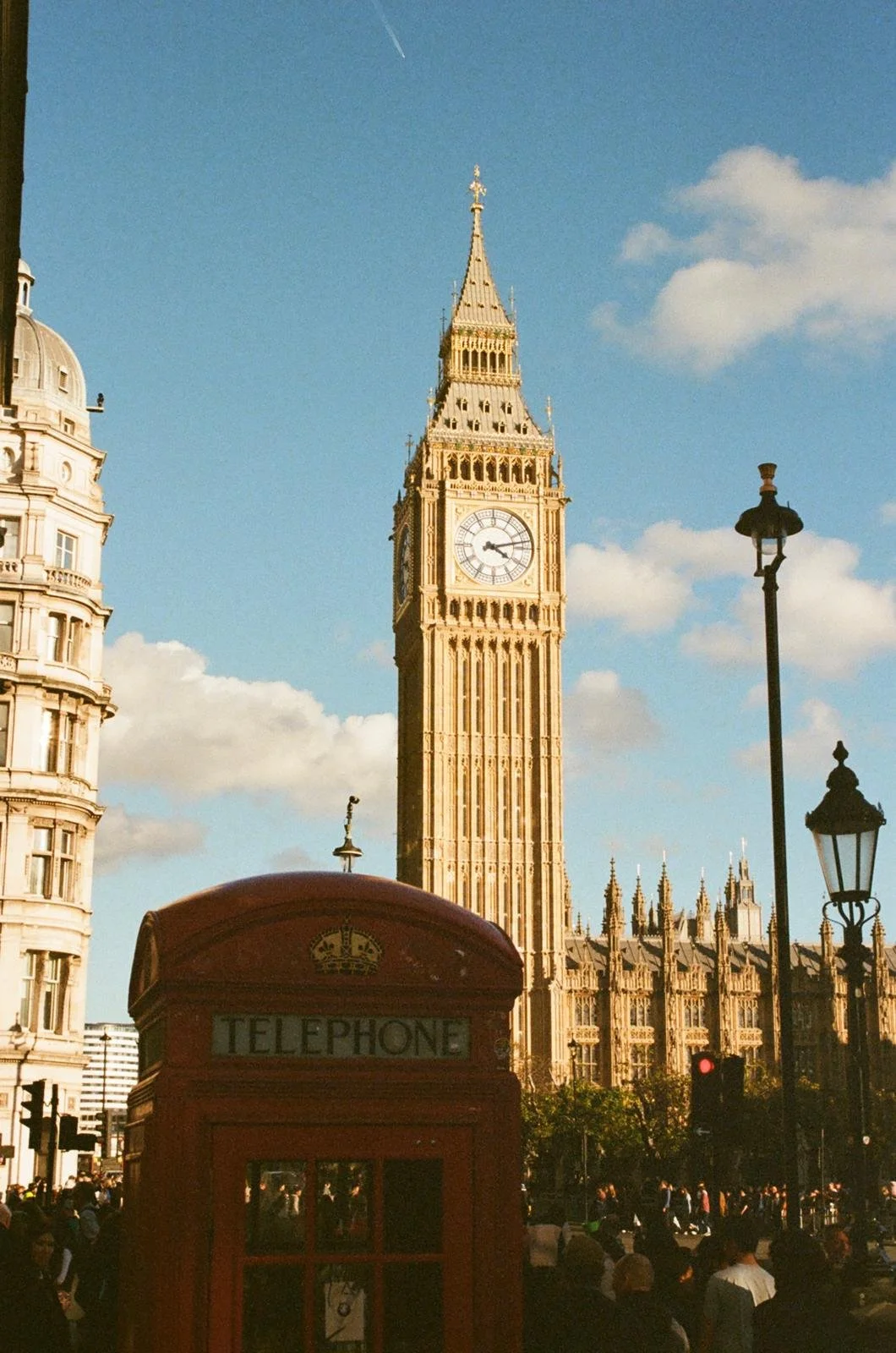 Big Ben clock tower in London with a red telephone booth in the foreground and a busy street with people below.