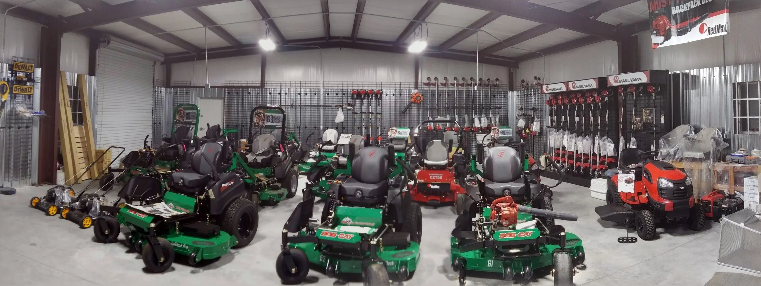 Indoor store displaying lawn equipment such as riding mowers, push mowers, and chainsaws, with metal shelves and tools in the background.