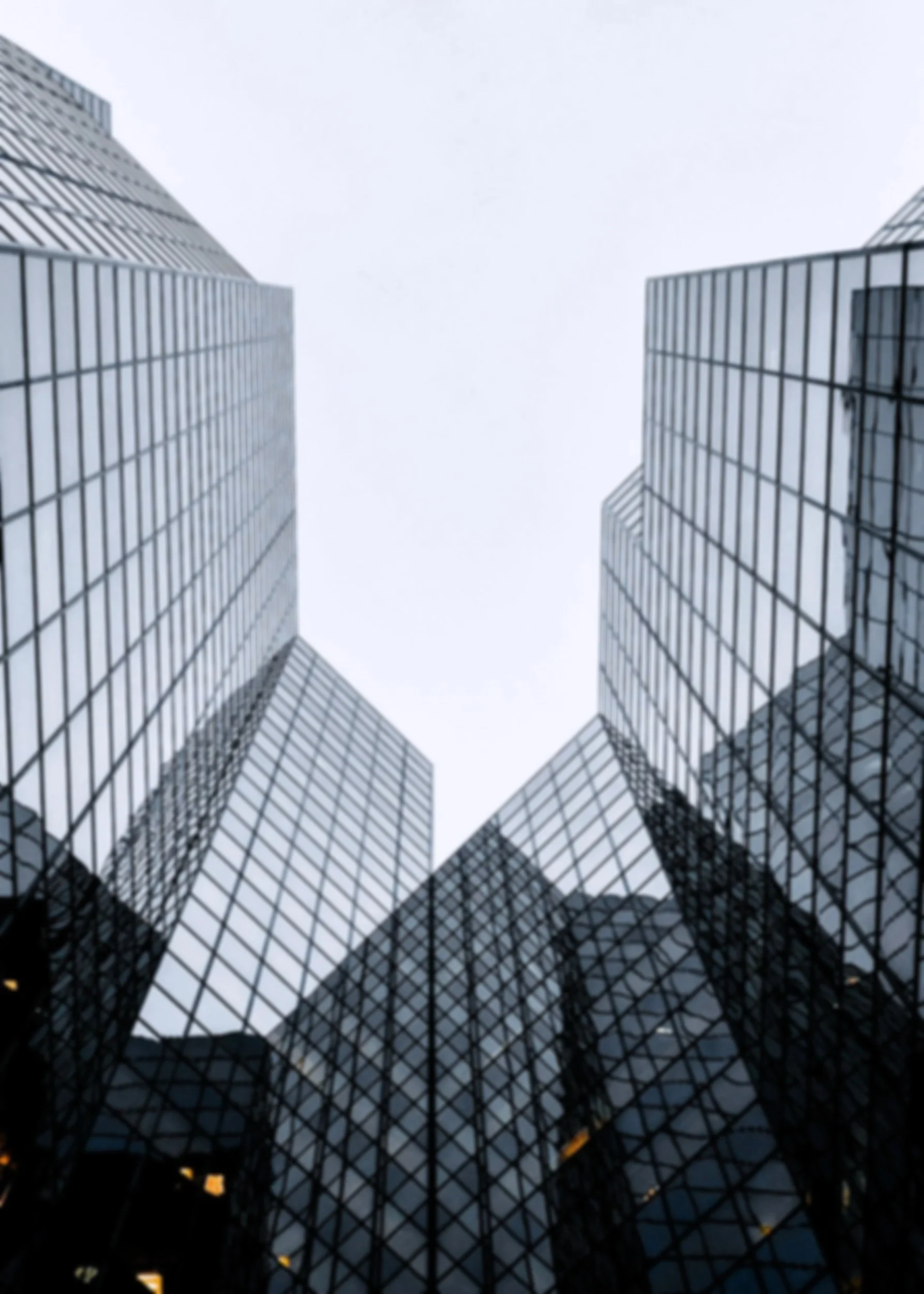 Looking up at modern glass skyscrapers with reflective windows in an urban cityscape.