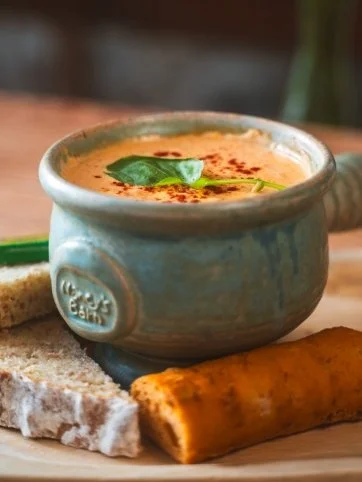 A bowl of award winning seafood chowder garnished with a basil leaf, served with homemade bread.