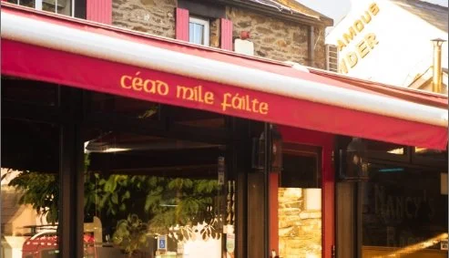 Red awning, stone building in the background, trees reflected in windows.
