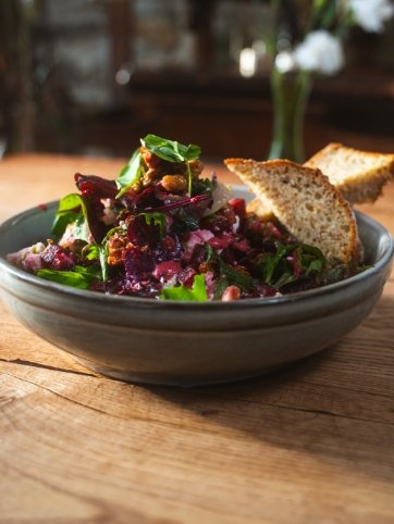 A bowl of mixed greens salad with cherry tomatoes, drizzled with dressing, topped with croutons, served with two slices of whole grain bread on the side.
