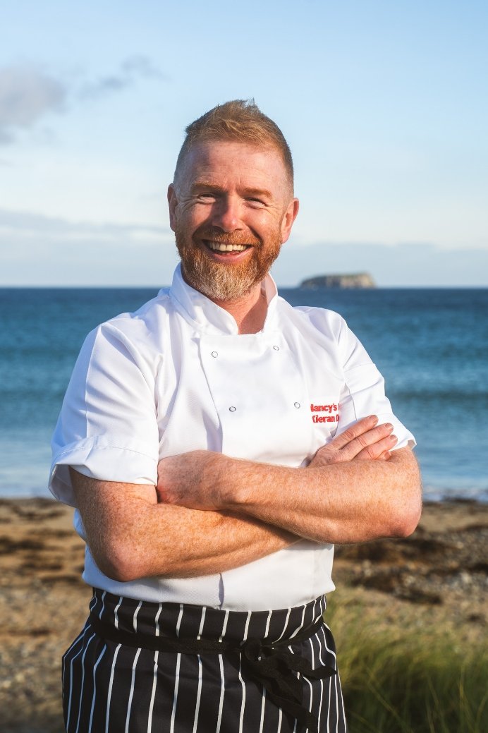 Kieran Doherty standing outdoors by the beach with arms crossed.