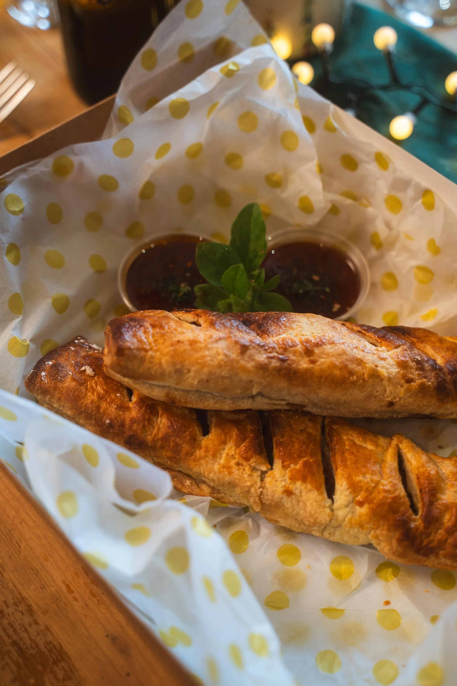 Two large golden sausage rolls in a paper-lined basket with a sticky dipping sauce