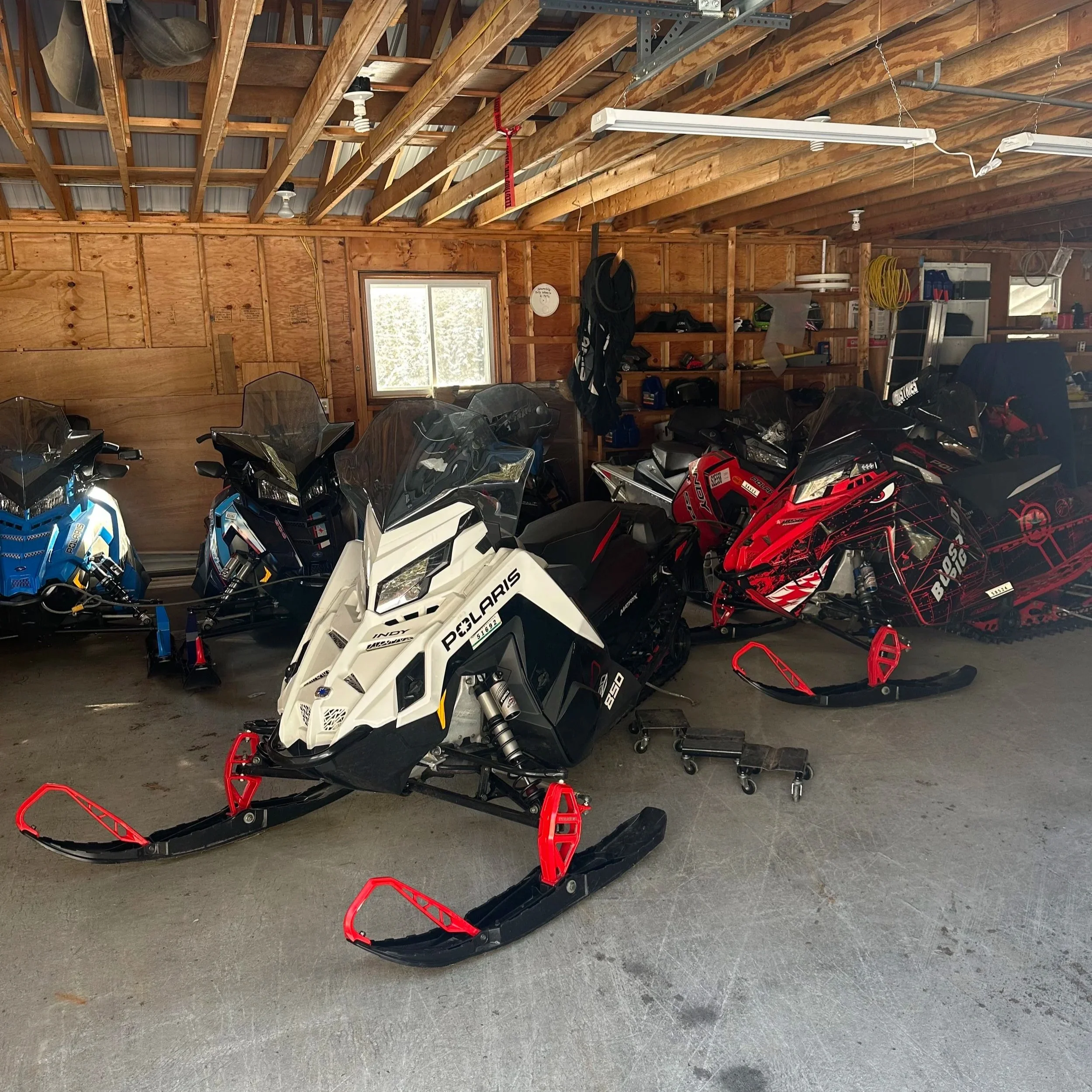 Several snowmobiles parked inside a wooden garage.