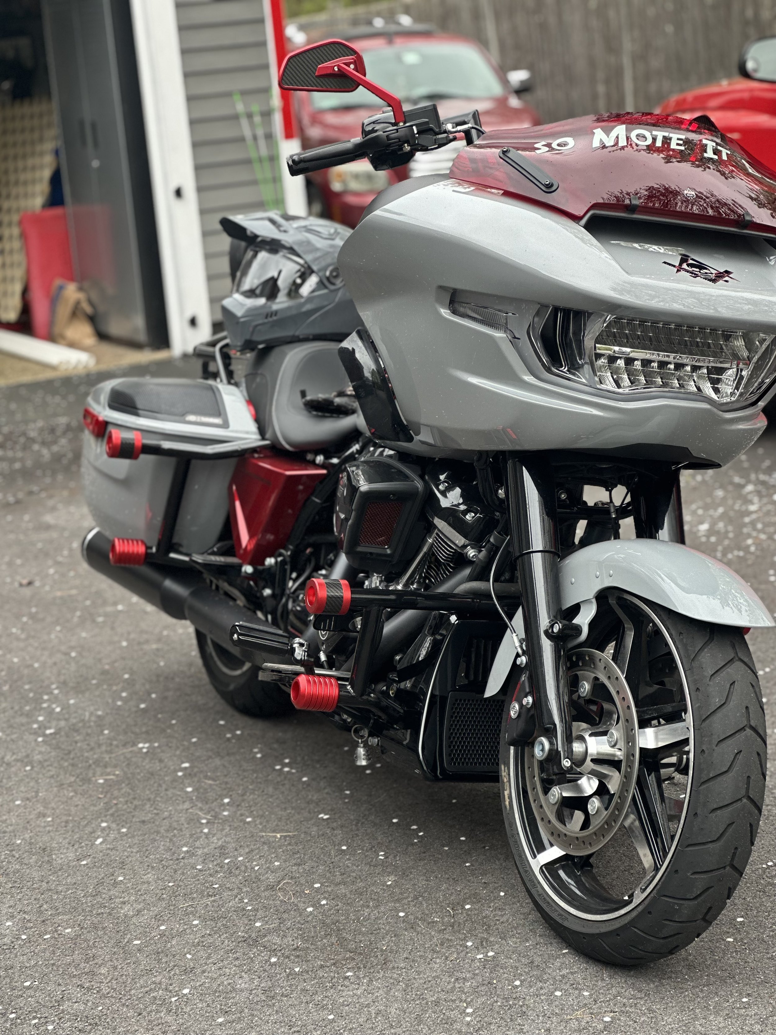 A modern motorcycle with a gray and red color scheme parked outside a building, featuring a large front fairing, disc brake on the front wheel, and custom red accents on the foot pegs and handle mirror.