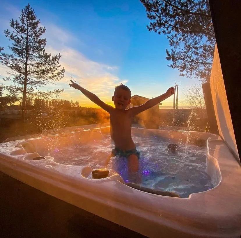 A child enjoying a jacuzzi in front of a sunset with trees in the background.