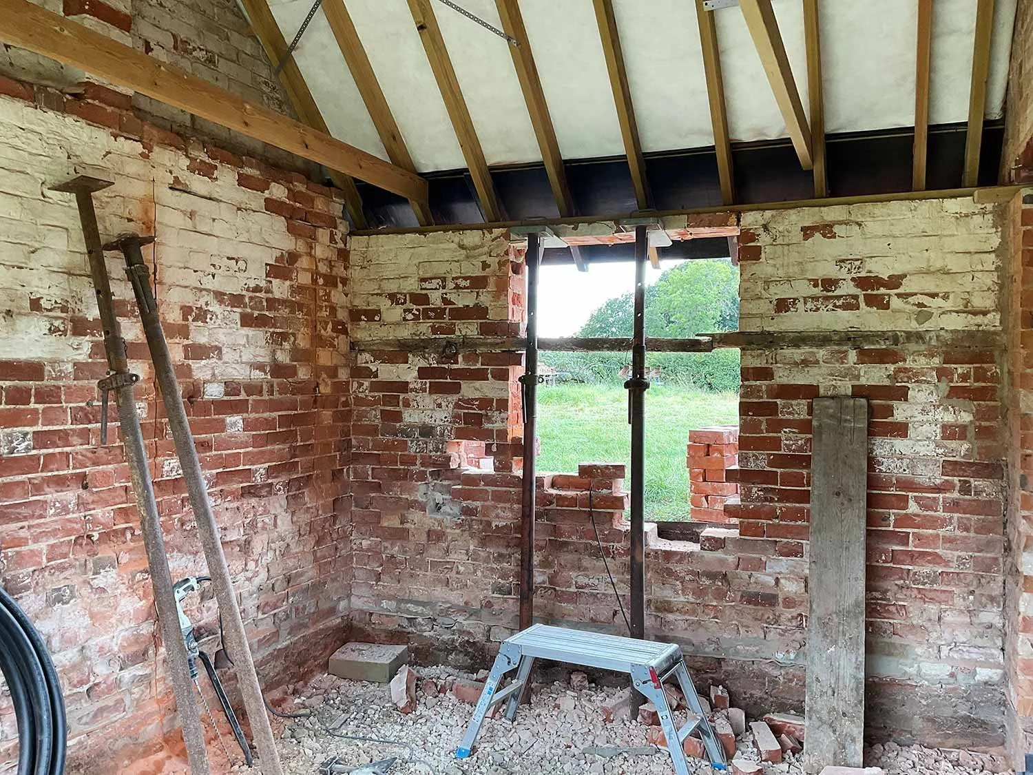 Brick barn interior mid-renovation with roof timbers exposed and space for original window.