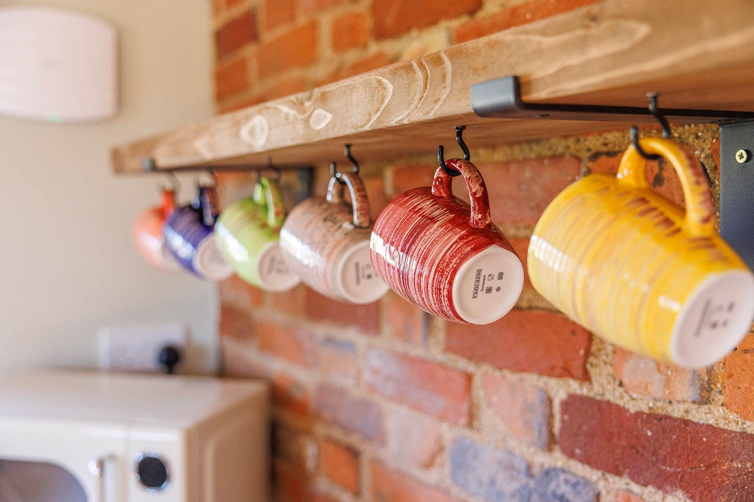 Colourful mugs hanging on rail against exposed brick wall.