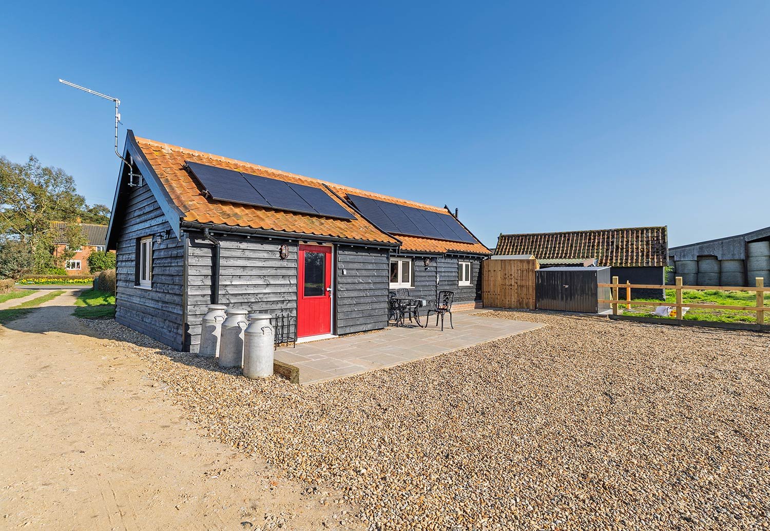 Converted dairy barn holiday let in rural Suffolk with red door and solar panels.