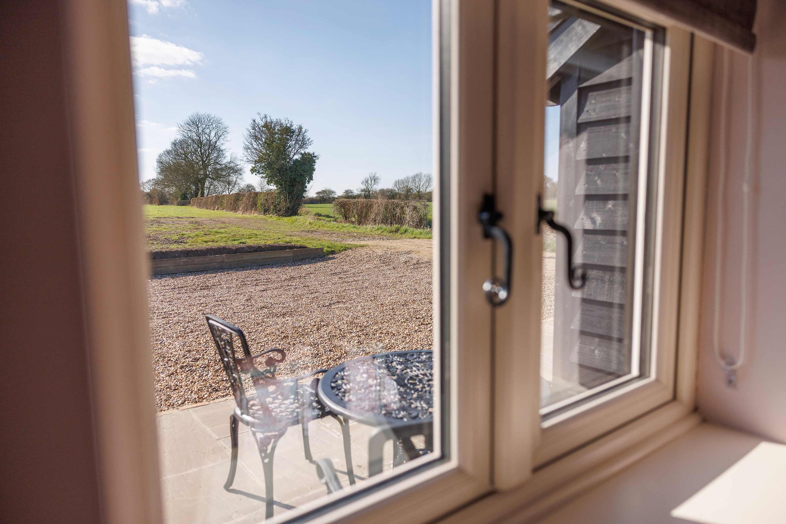 View through window to outdoor seating and countryside.